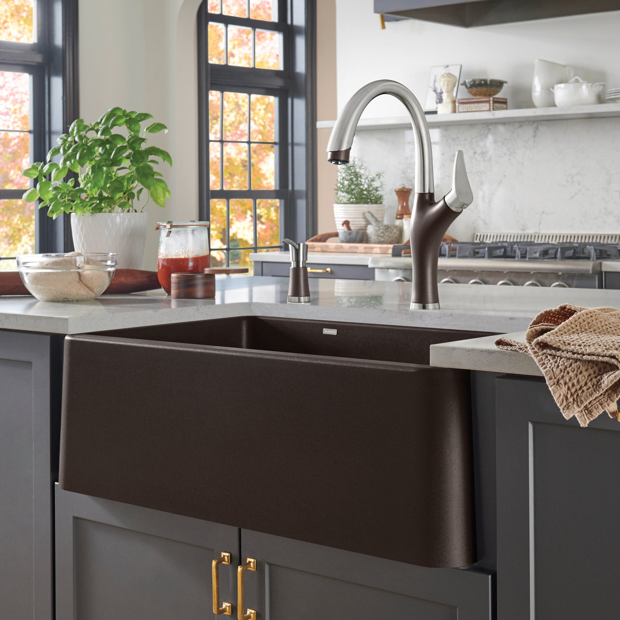Cafe brown apron front farmhouse sink with curved stainless steel faucet installed in gray cabinetry.
