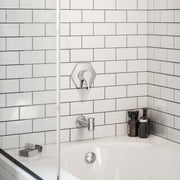 Chrome tub spout with diverter mounted on white subway tile above a bathtub.