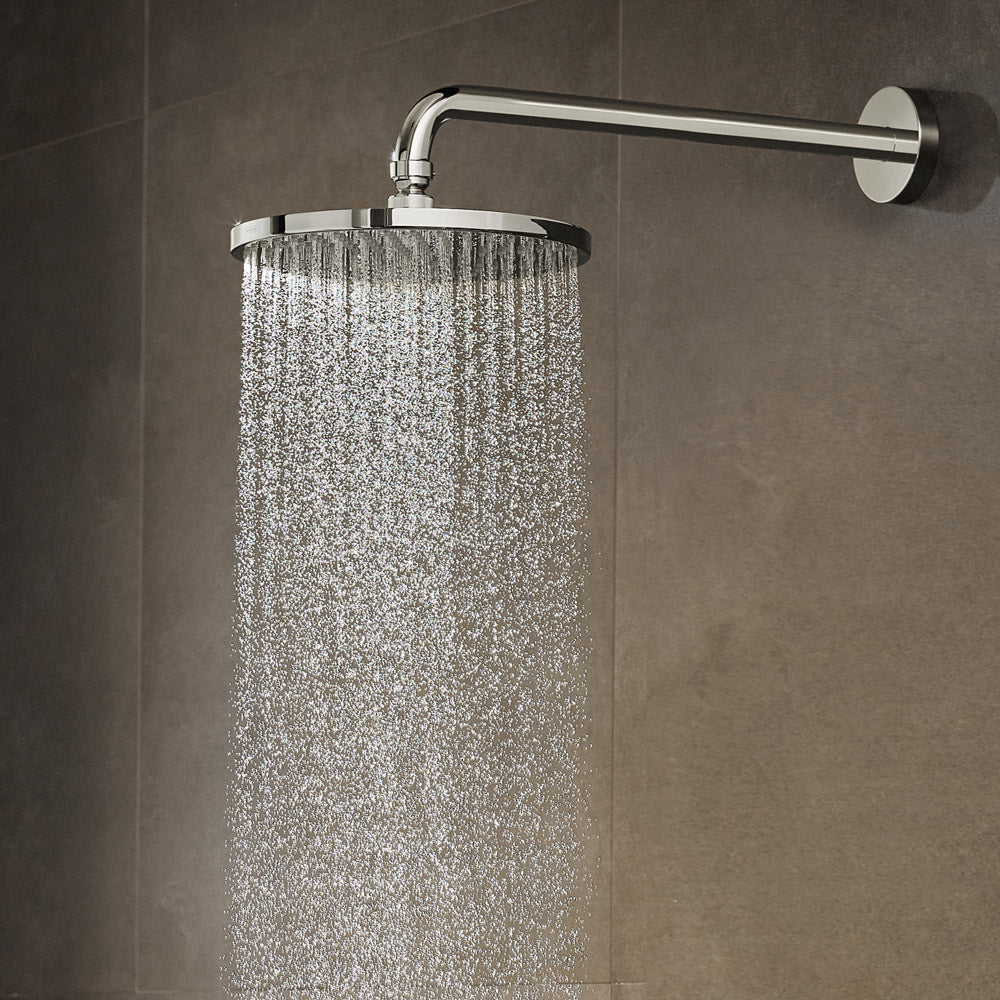 Brushed nickel circular shower head with wall-mounted arm dispensing water spray against gray tile.