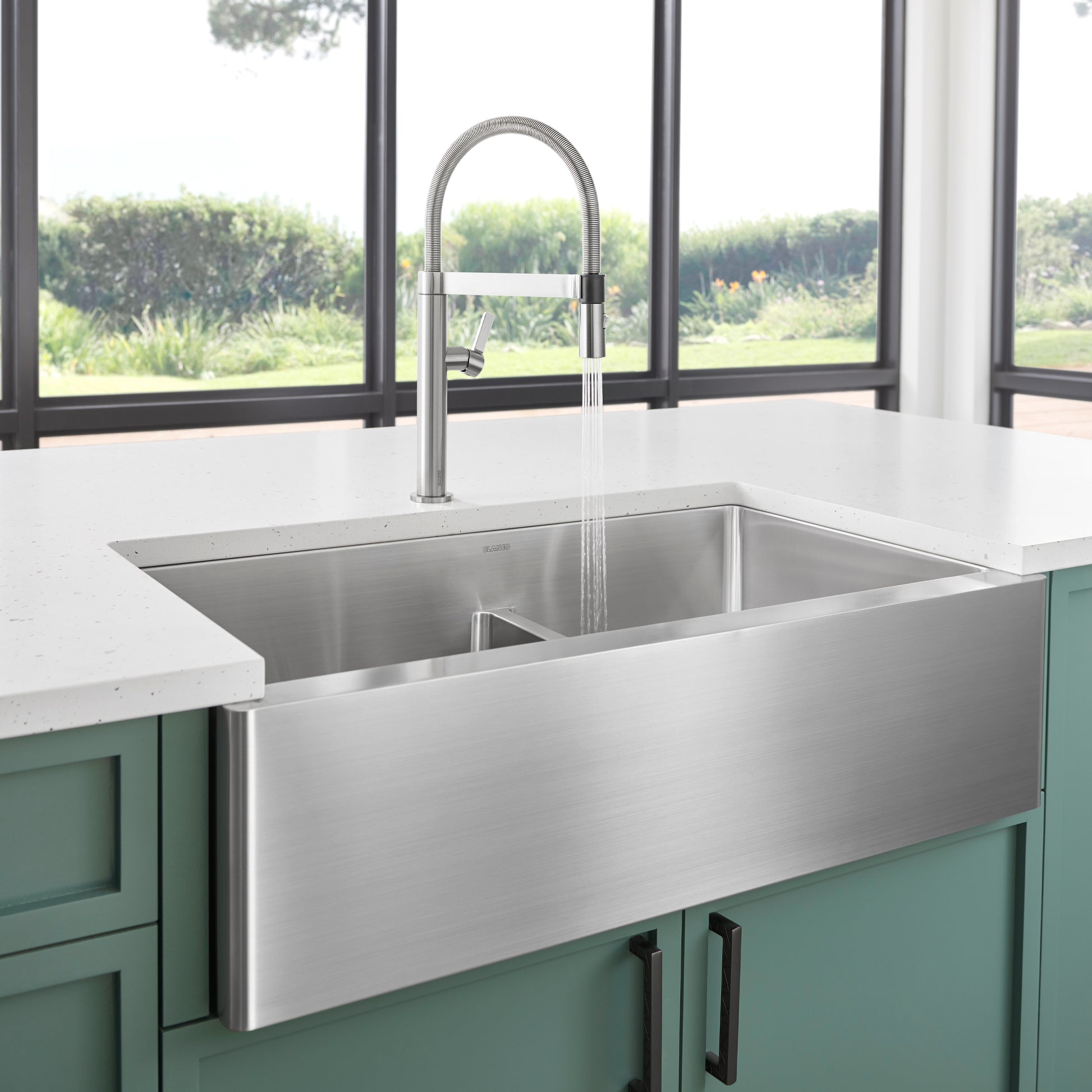 Stainless steel apron front sink with two compartments and low divide, paired with chrome pull-down faucet.