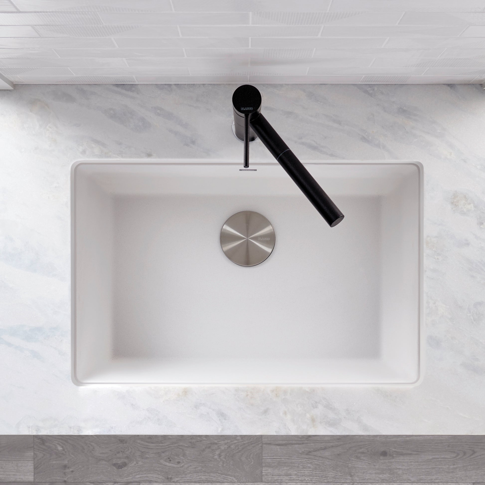White rectangular kitchen sink with single bowl, stainless steel drain, and black faucet, viewed from above on marble counter