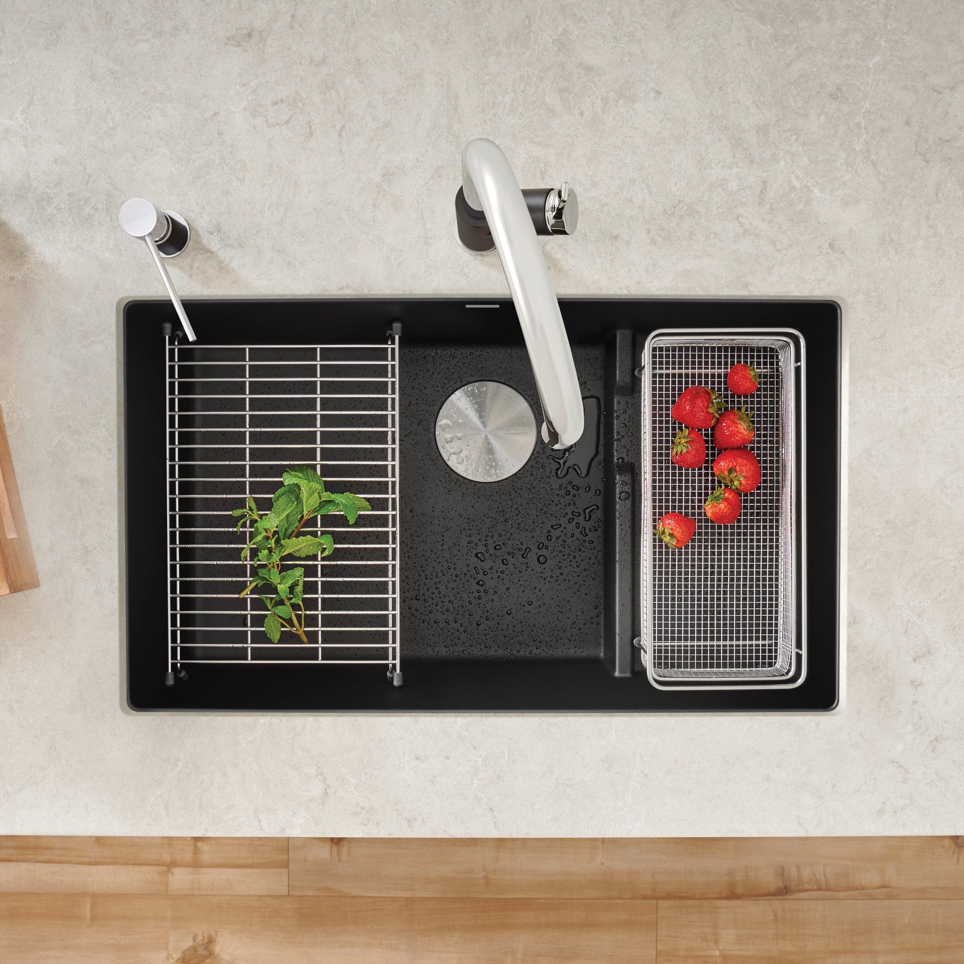 Coal black single kitchen sink with white faucet, colander, and metal grid insert containing fresh produce.