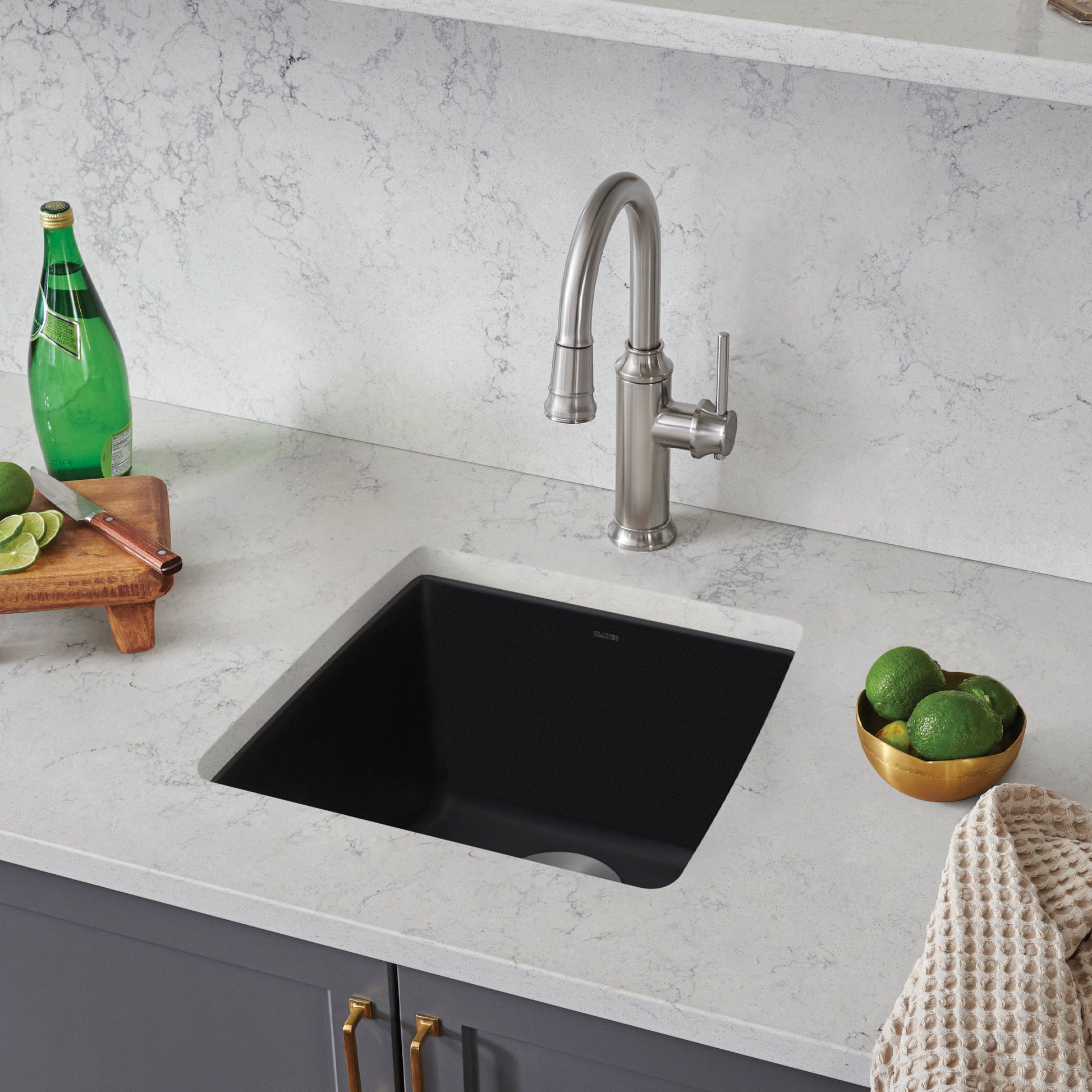 Coal black undermount bar sink with stainless steel faucet installed in marble countertop.