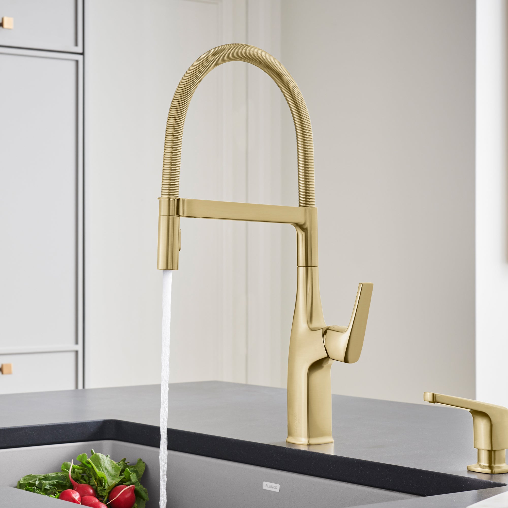 Satin gold semi-pro kitchen faucet with flexible hose sprayer and single handle lever, water running into sink.