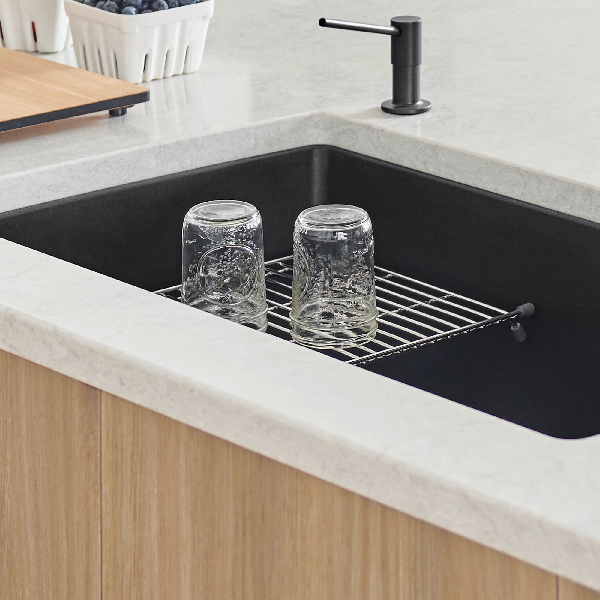 Stainless steel sink grid with parallel bars positioned in black undermount kitchen sink holding two glass jars.