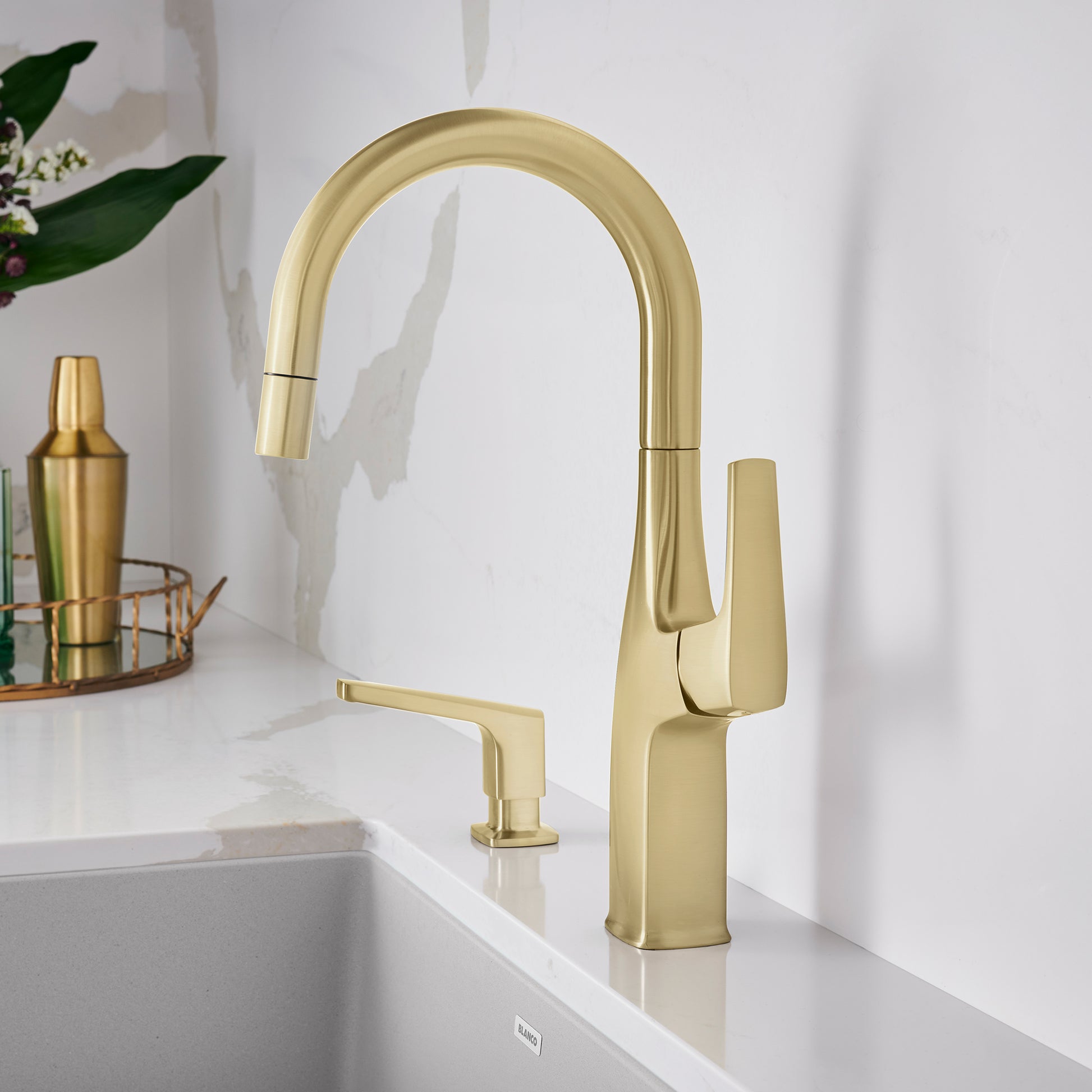 Satin gold bar faucet with high arched spout and single lever handle above white sink.