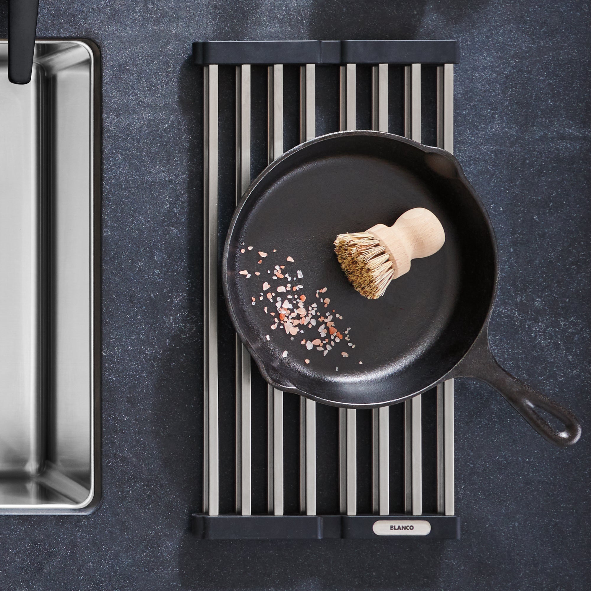 Black and white striped foldable drying mat with skillet and brush on dark countertop.