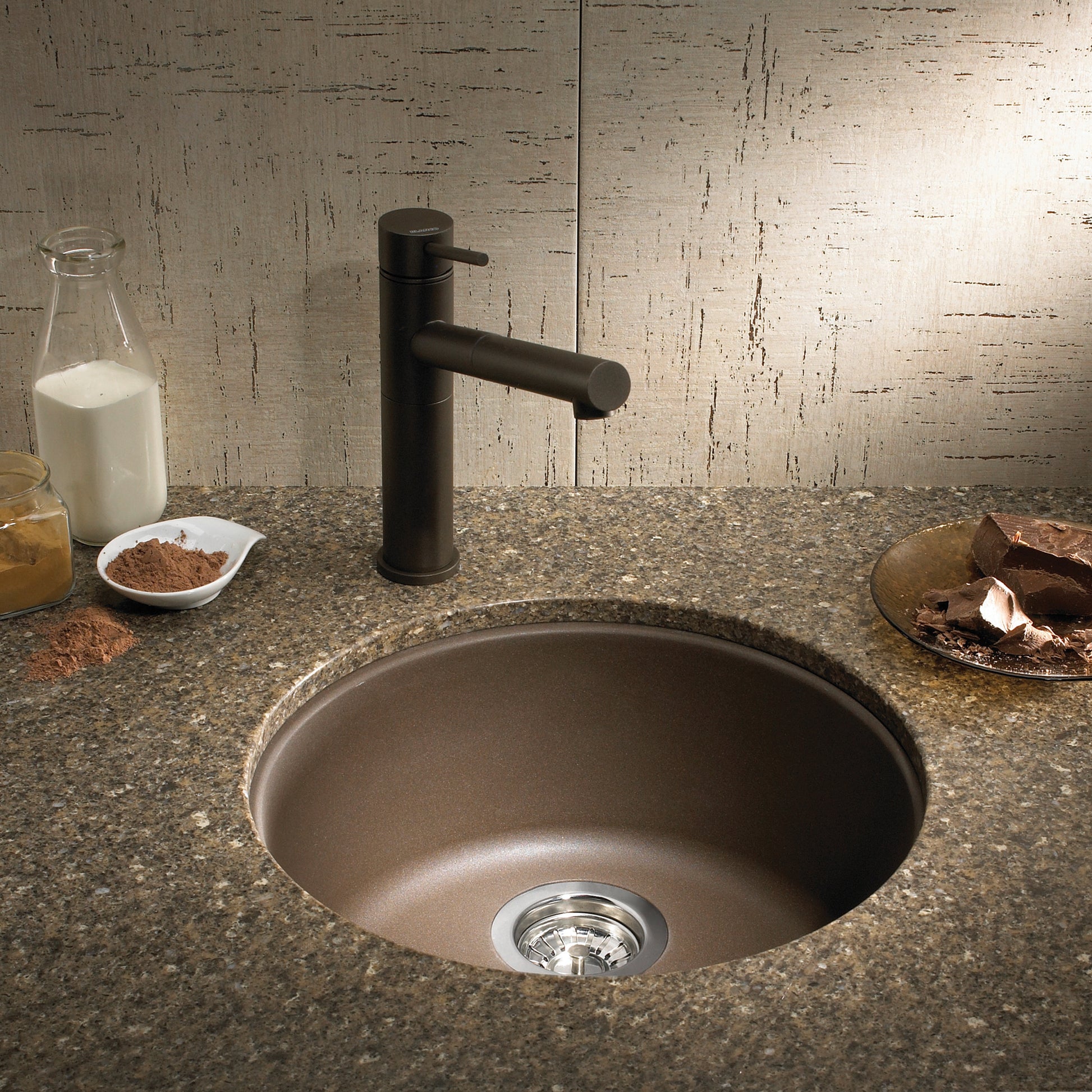 Cafe brown undermount bar sink with rounded basin and black faucet installed in speckled countertop.