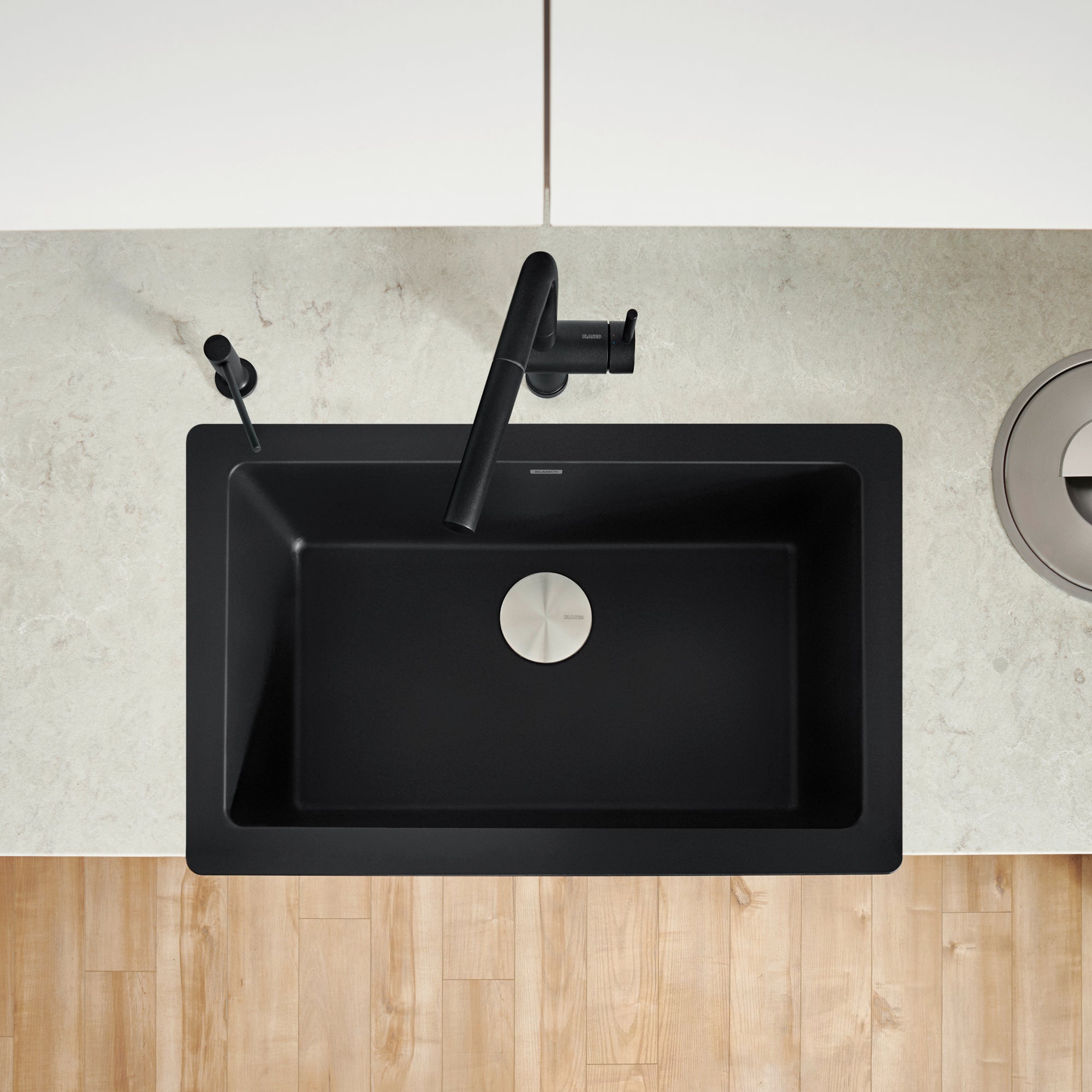 Coal black farmhouse sink with single basin, apron front, and black faucet with matching spray attachment, viewed from above.