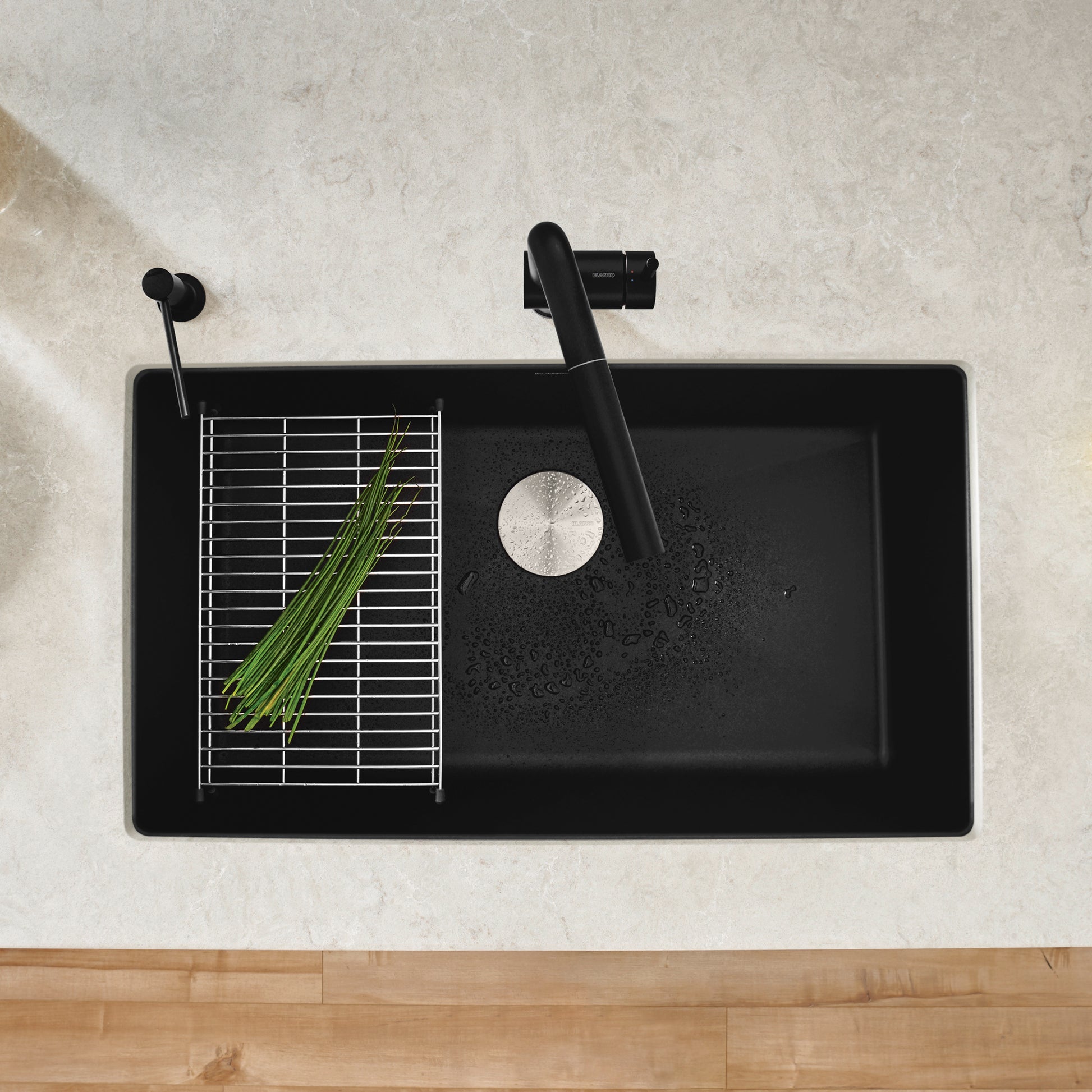 Coal black single bowl kitchen sink with integrated drain board, metal grate, and black faucet, viewed from above.