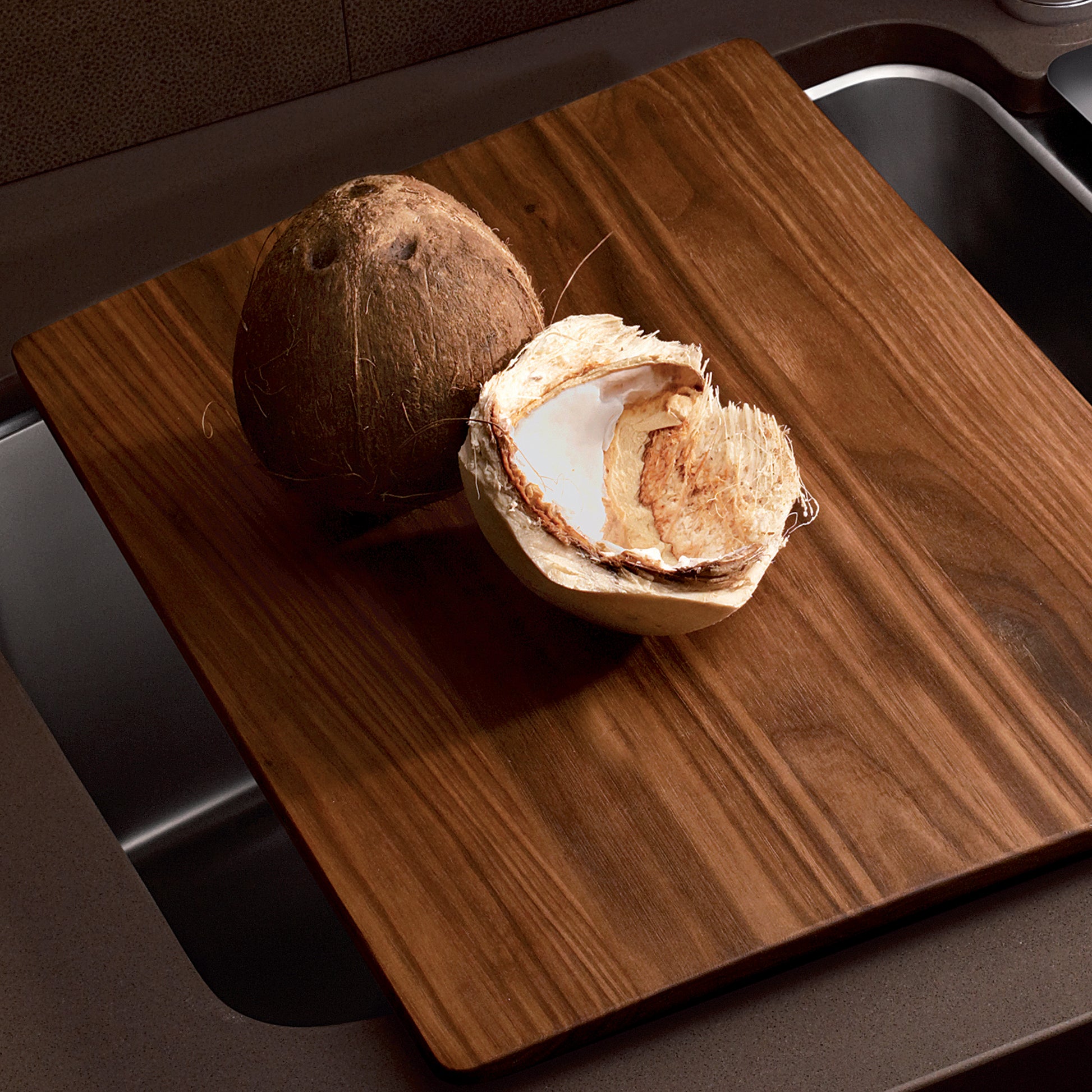 Medium rectangular wood cutting board with vertical grain pattern displayed on dark countertop with coconut.