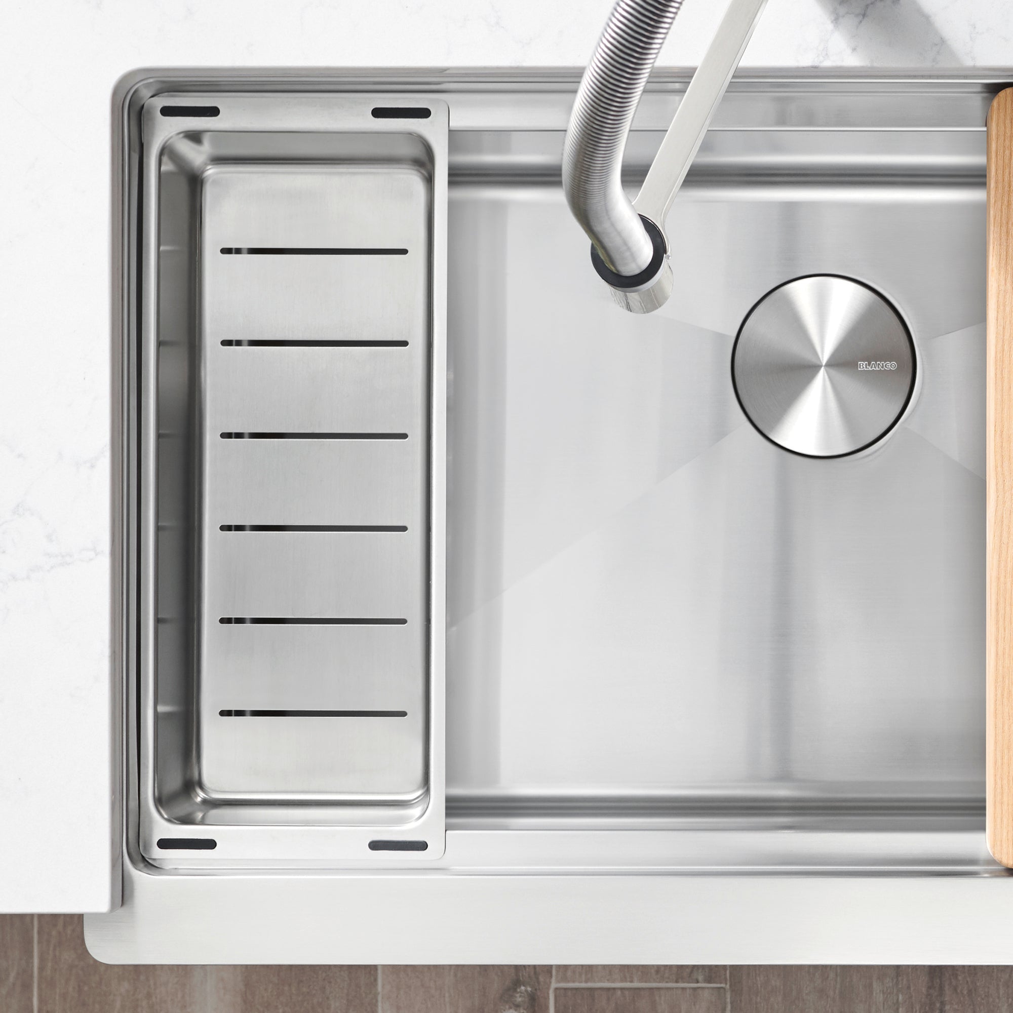Stainless steel colander with parallel slats installed in kitchen sink basin next to circular drainer.