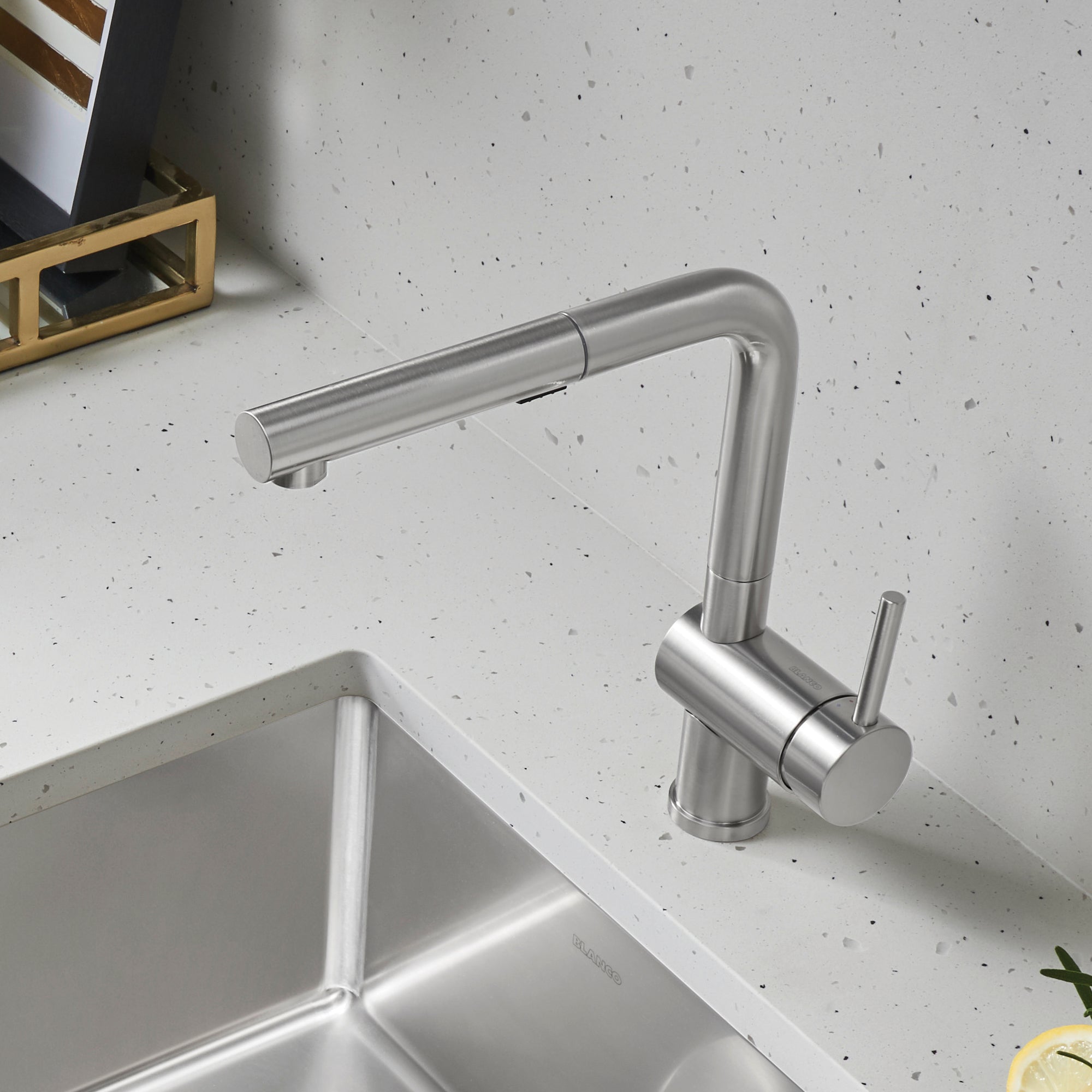 Stainless steel pull-out kitchen faucet with single handle and curved spout over white sink.