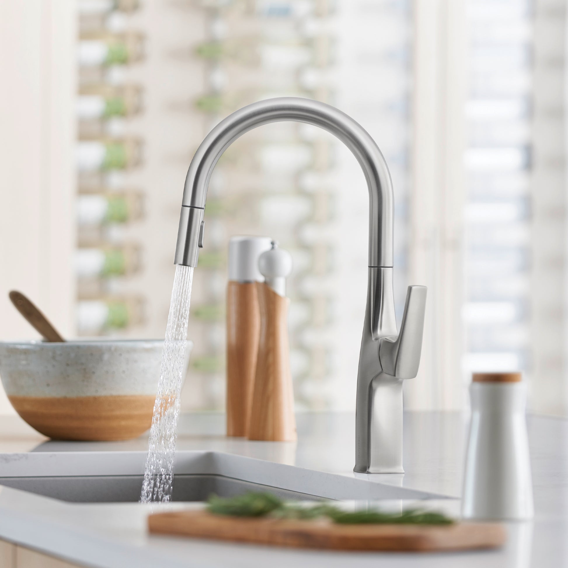 Stainless steel pull-down kitchen faucet with curved spout and single lever handle, shown installed over a sink with water fl