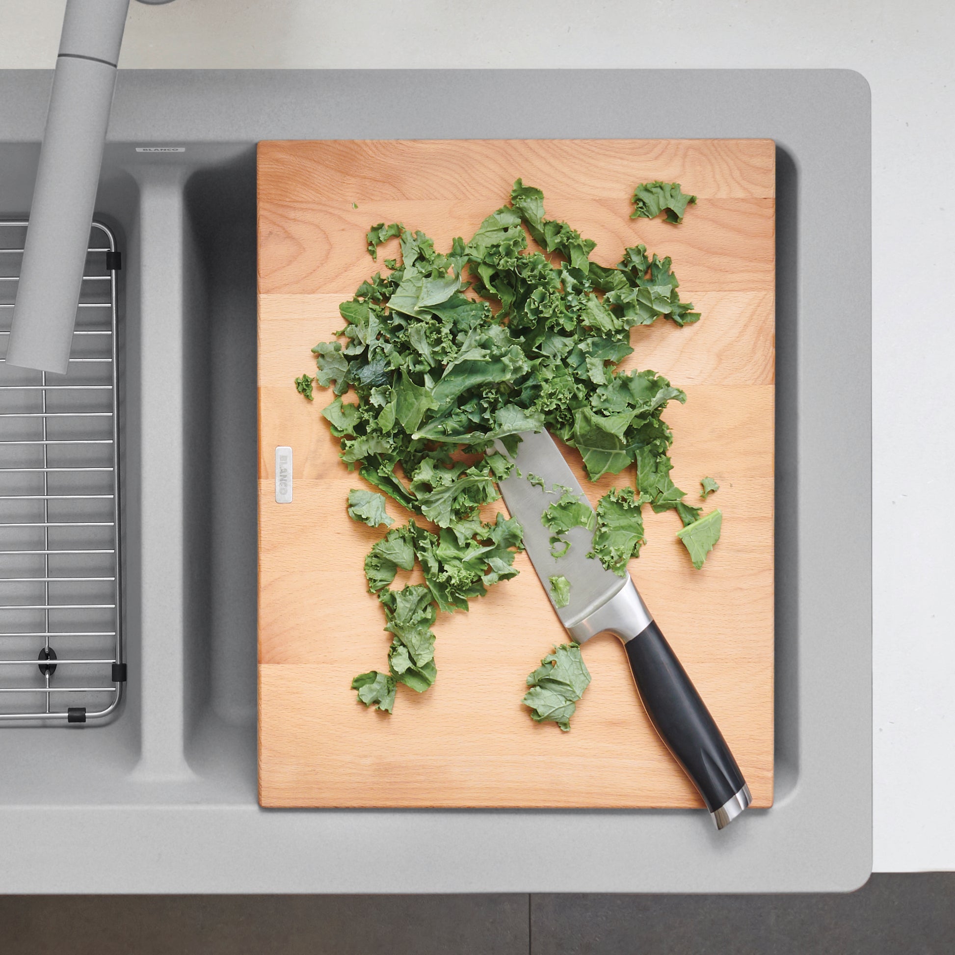 Beechwood cutting board with chopped kale and knife positioned on gray apron front sink.