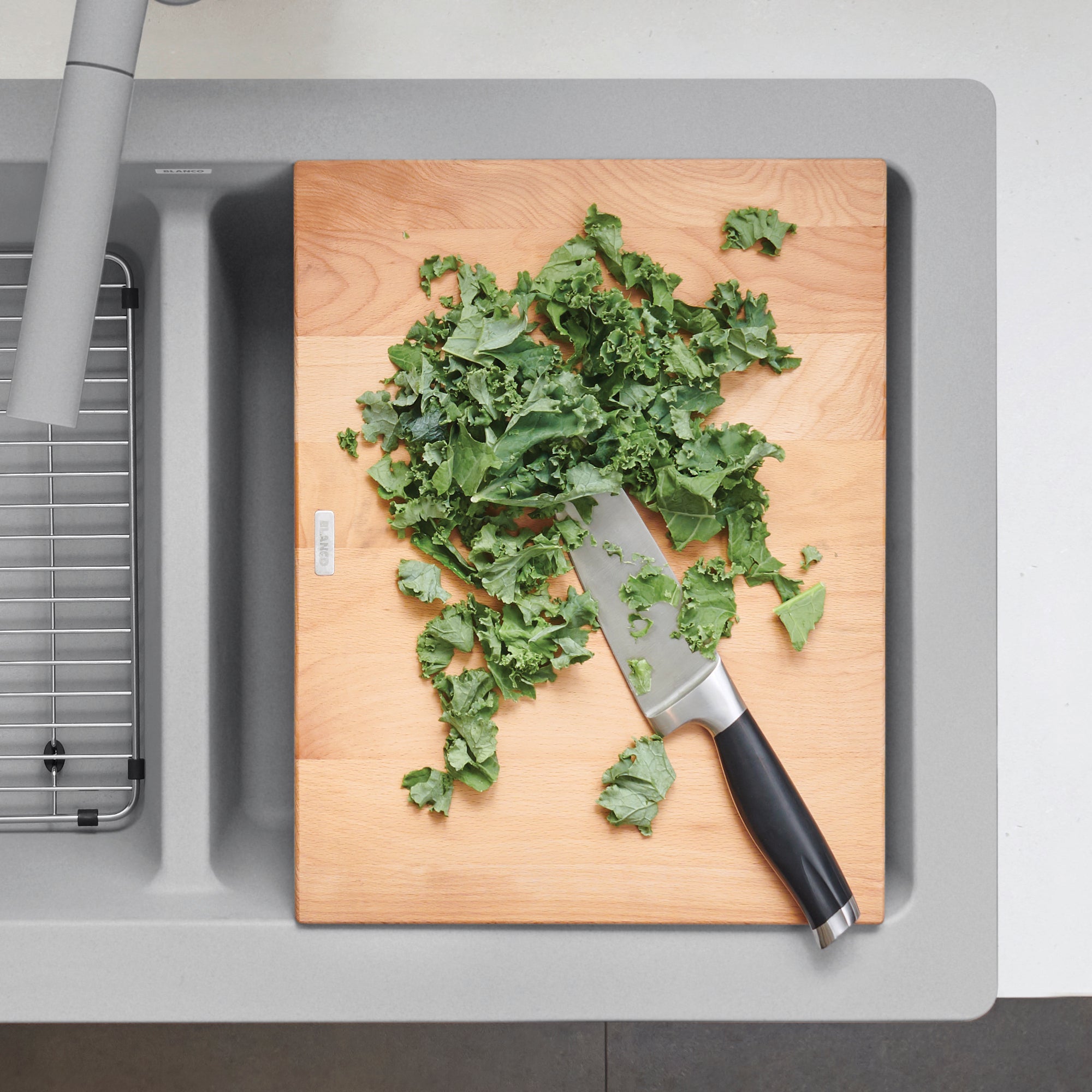 Beechwood cutting board with chopped kale and knife positioned on gray apron front sink.