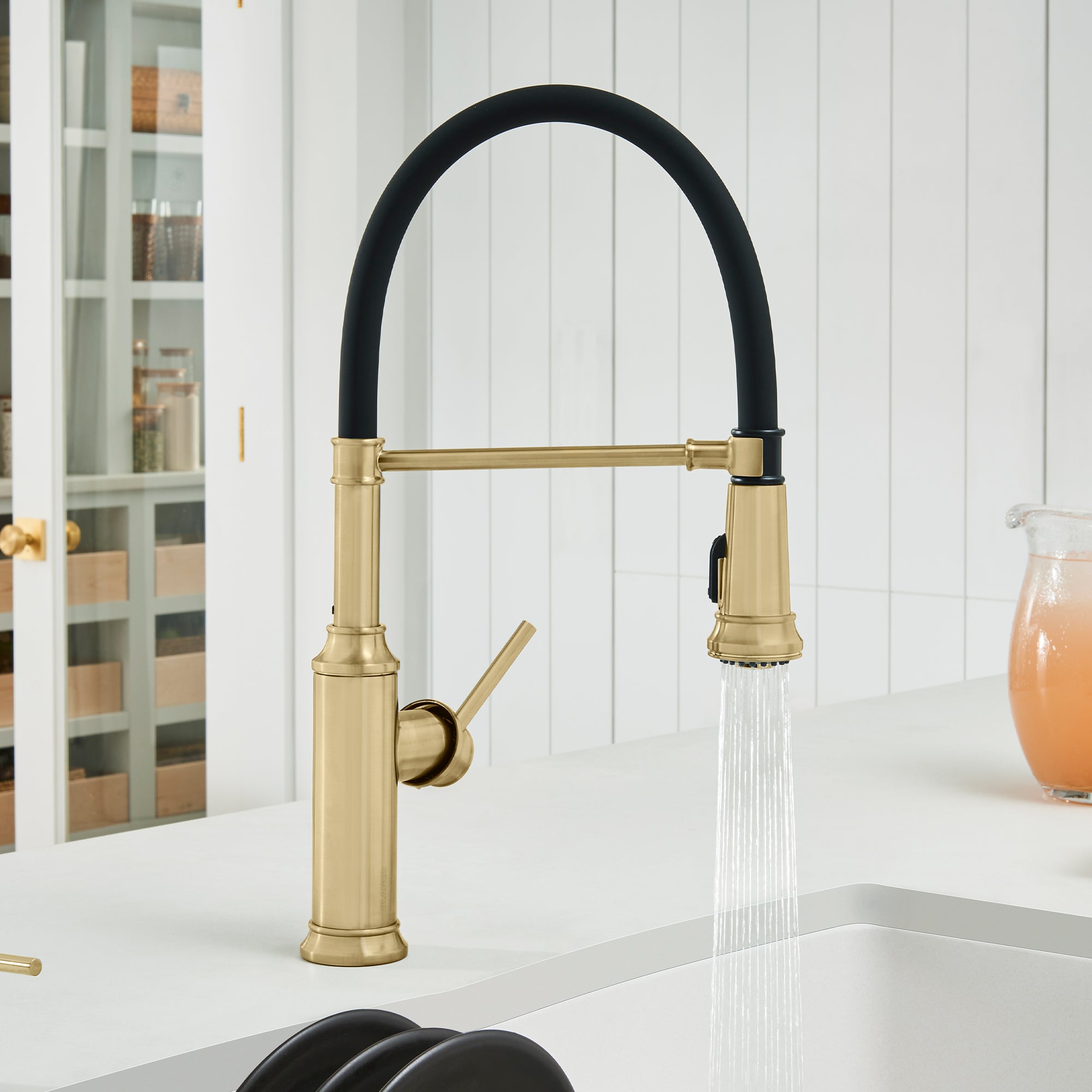 Satin gold semi-pro kitchen faucet with black coiled hose, single lever handle, and pull-down spray head over sink.