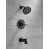 Matte black tub spout and two round trim rings mounted on gray tile wall.