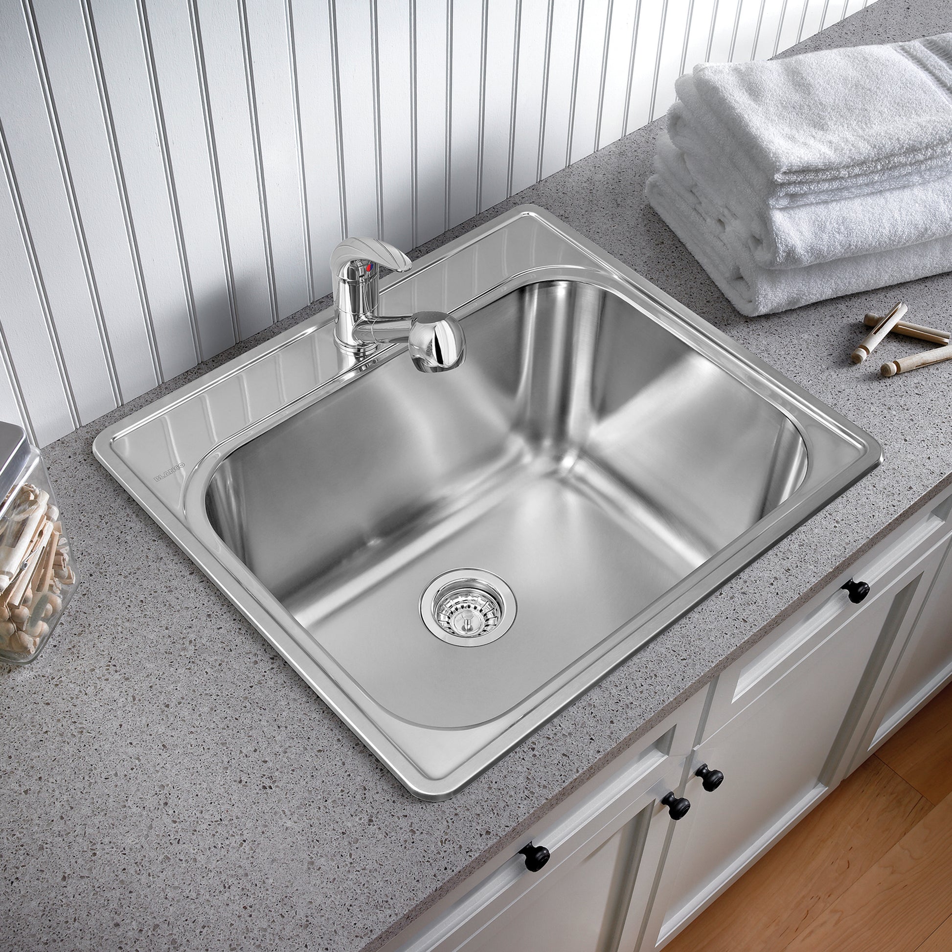 Stainless steel laundry sink with single faucet hole, drain strainer, and chrome faucet installed on gray countertop.
