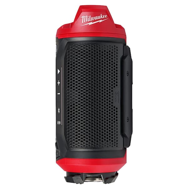 Red and black Milwaukee jobsite speaker with perforated grille front, control buttons on side, and PACKOUT base attachment.