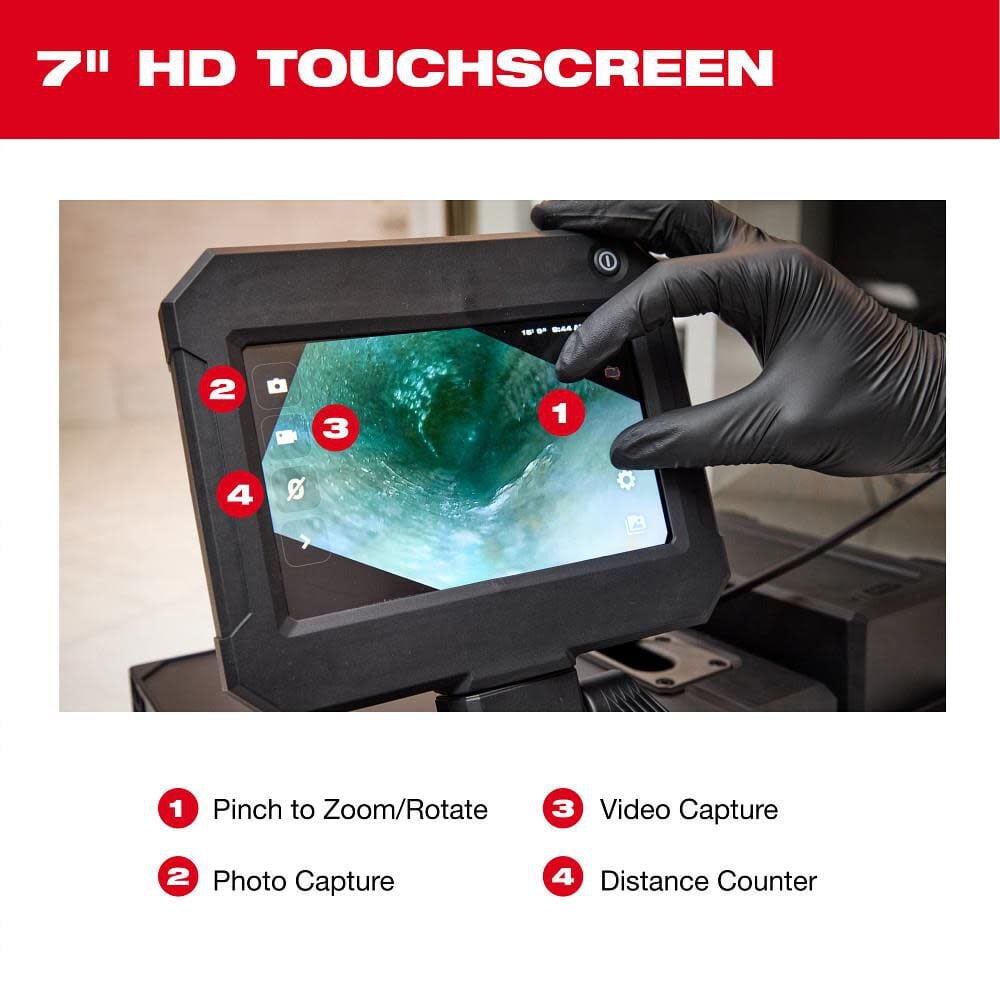 Hand holding drain camera monitor displaying interior pipe inspection with 7-inch touchscreen showing green debris accumulati