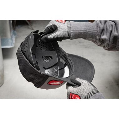 Black plastic bump cap insert with ventilation holes and red accents, held in gloved hands.