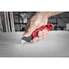 Red and black folding utility knife with blade storage compartment on concrete surface.