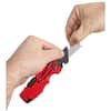 Red folding utility knife with tan handle held open in hand.