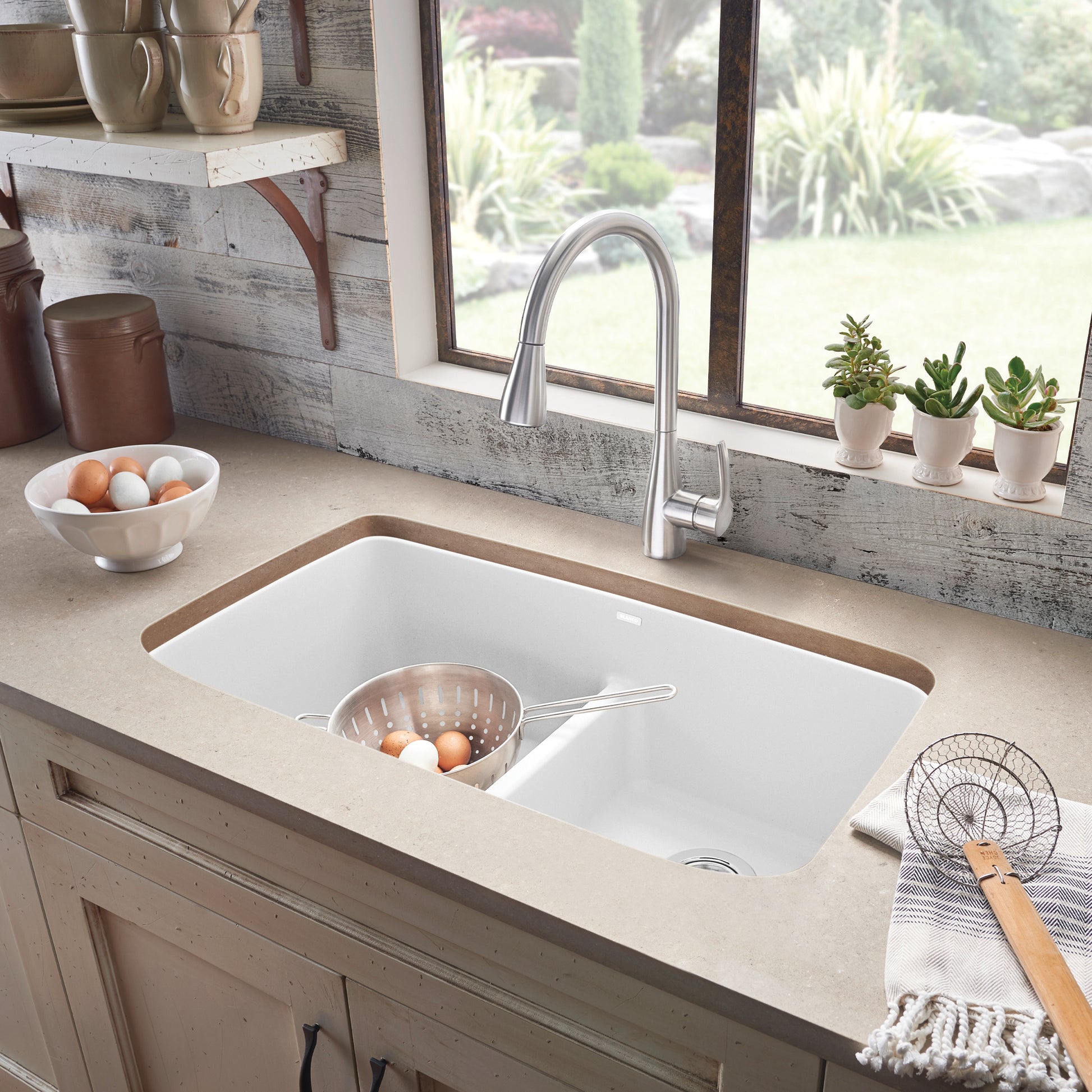 White double undermount kitchen sink with low divider, silver faucet, and colander in left basin.
