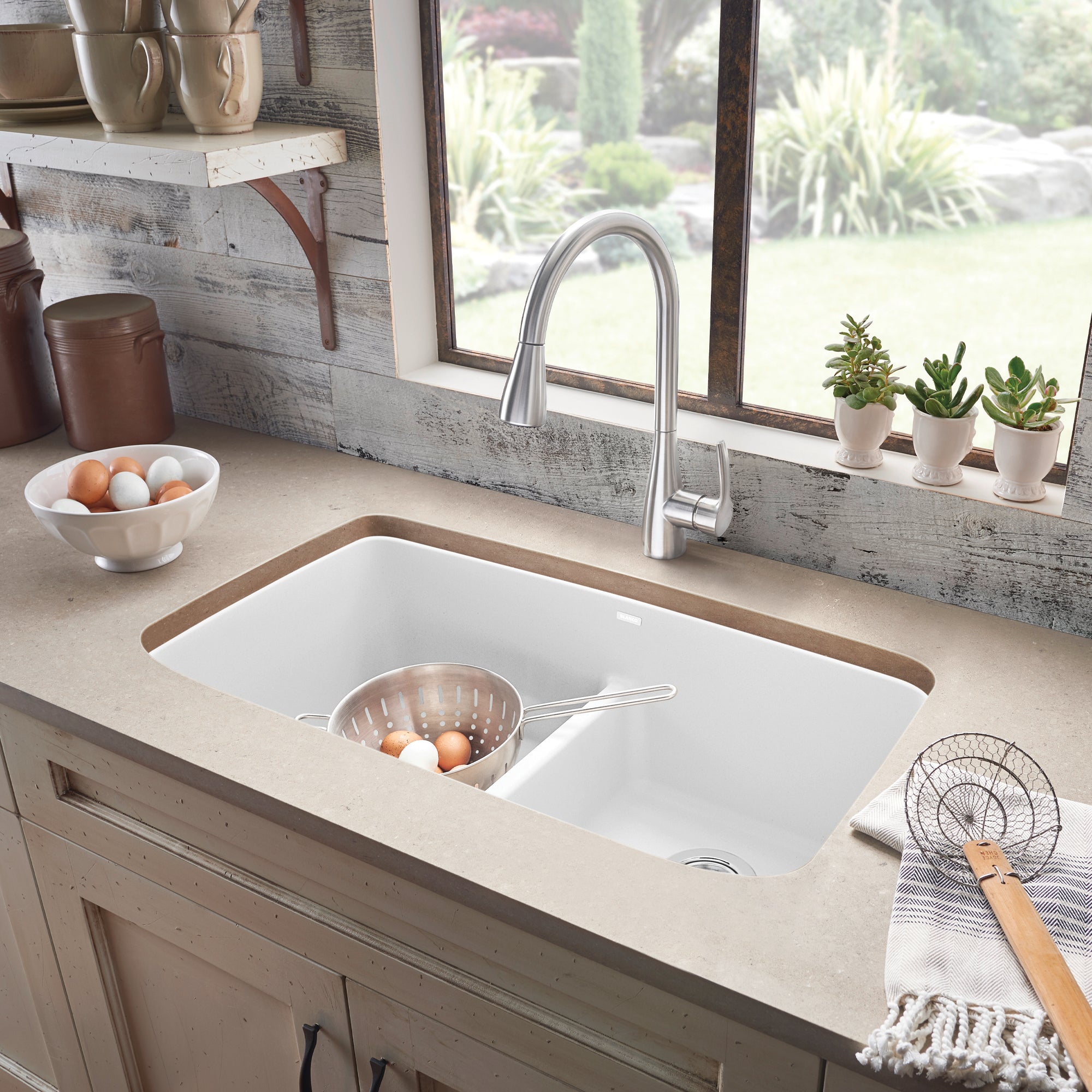 White double undermount kitchen sink with low divider, silver faucet, and colander in left basin.