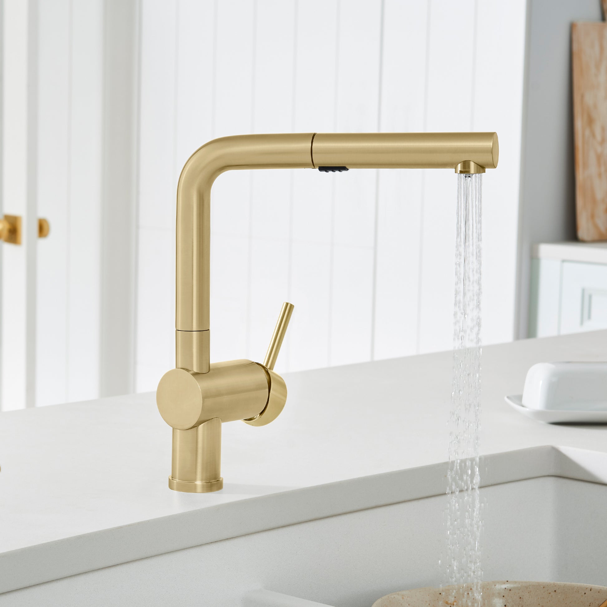 Satin gold pull-out kitchen faucet with single lever handle and extended spout, water flowing from pulled-out spray head.