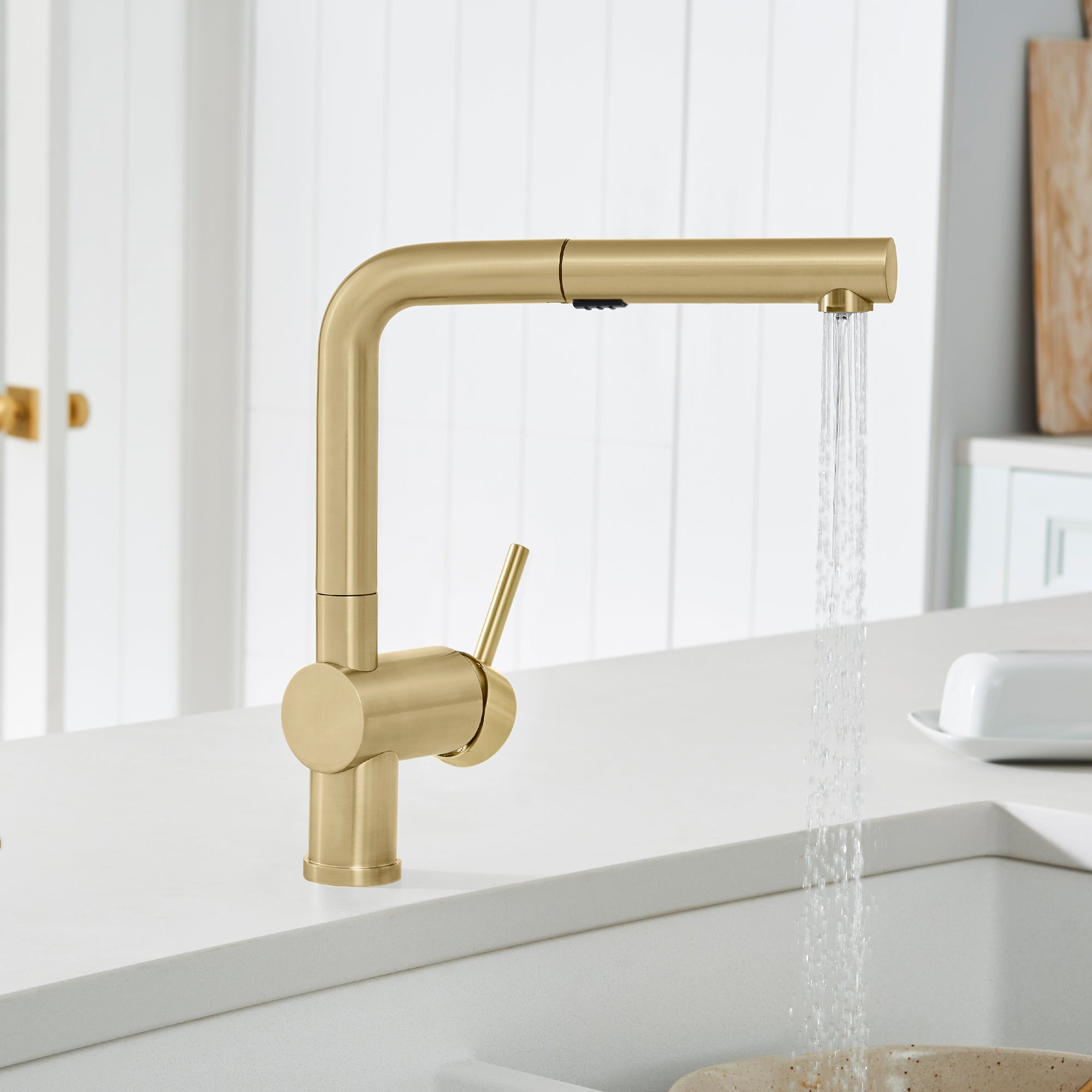 Satin gold pull-out kitchen faucet with single lever handle and extended spout, water flowing from pulled-out spray head.