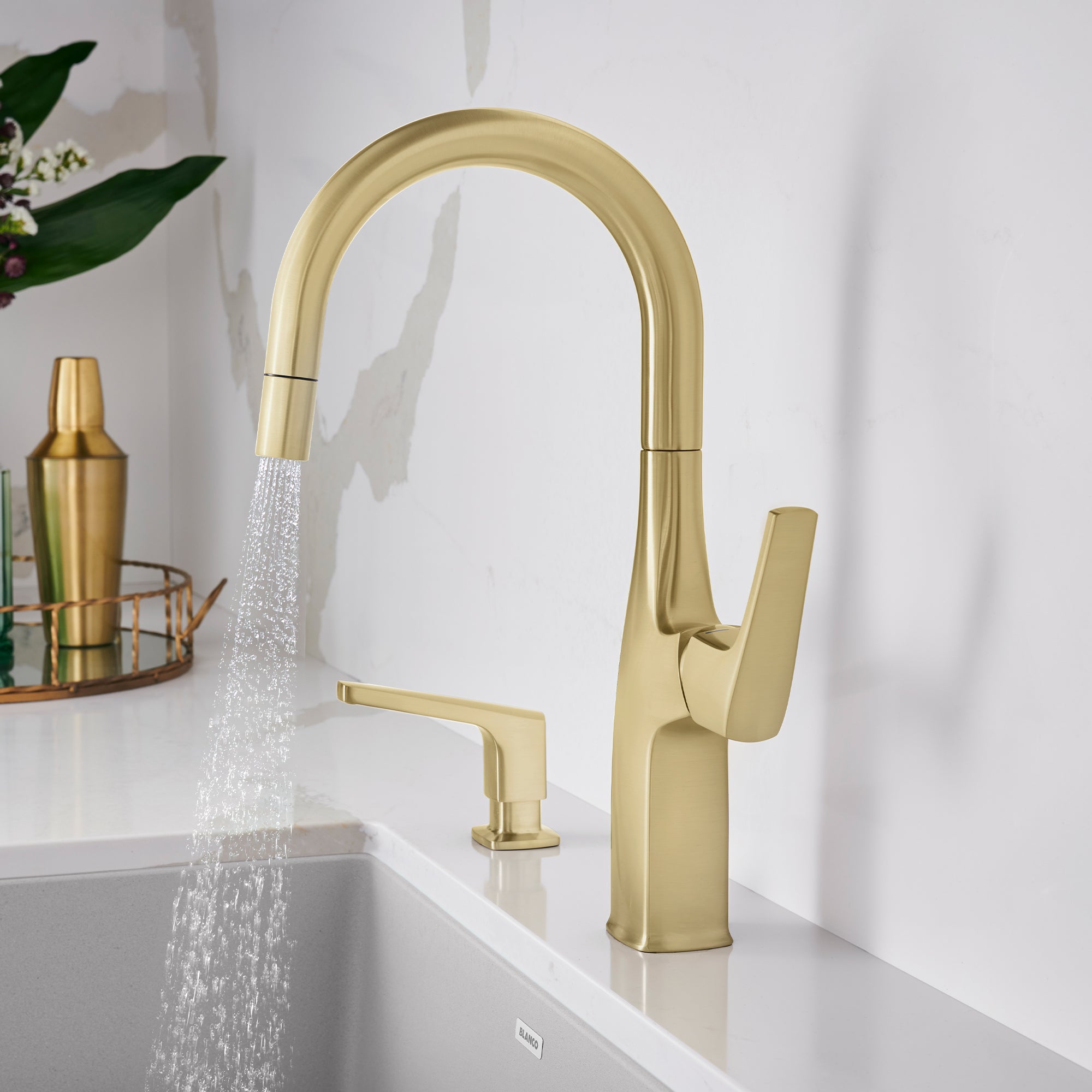 Satin gold bar faucet with curved spout, single handle lever, and spraying water stream over white sink.