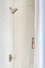 Polished nickel round shower head mounted on white subway tile wall with control valve below.