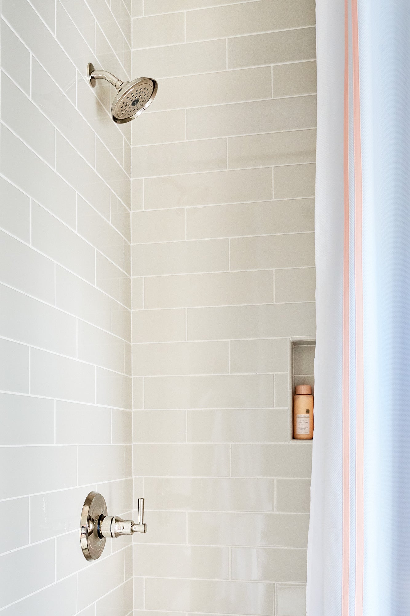 Polished nickel shower head with round face and spray holes mounted on white subway tile wall above control valve.