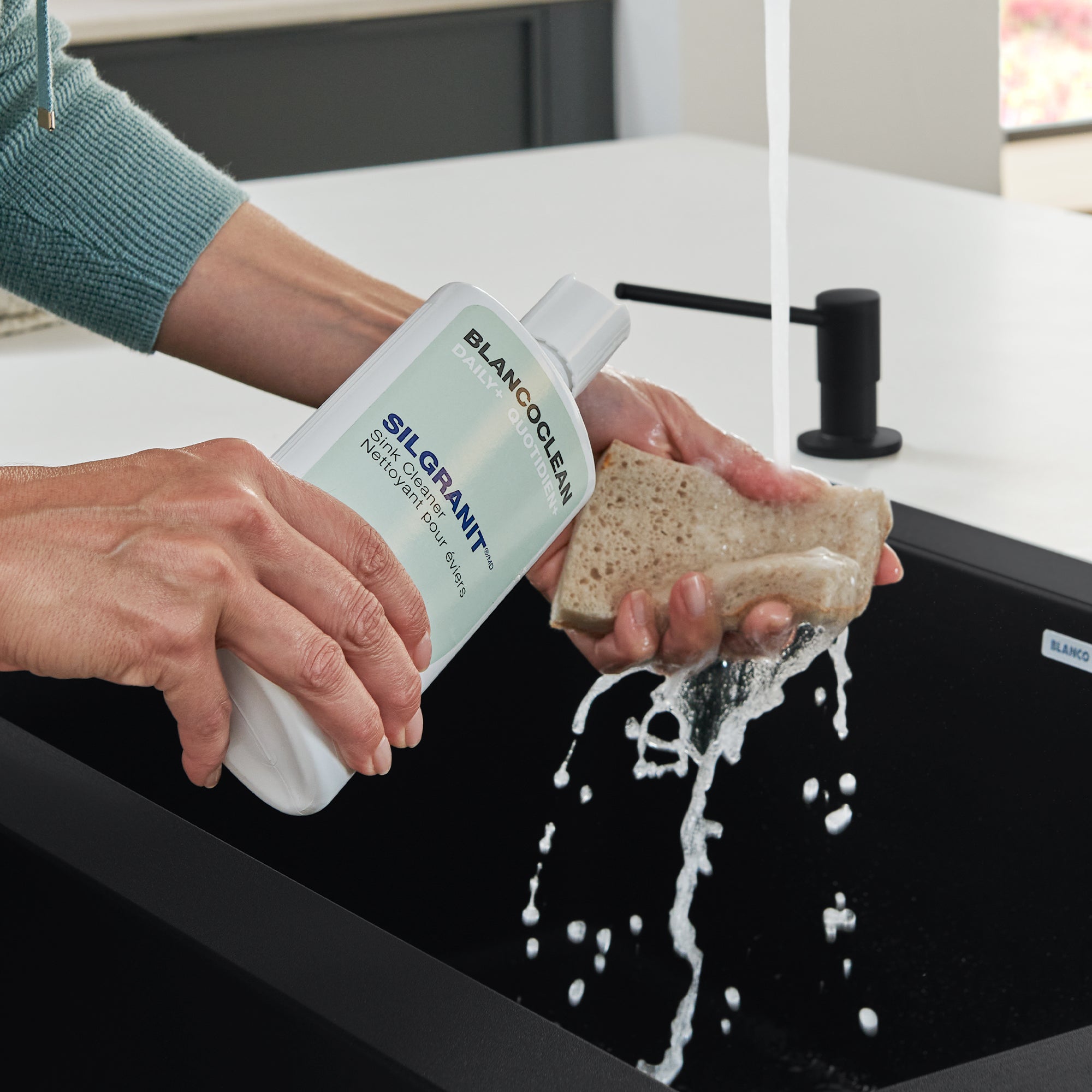 Blanco silgranit sink cleaner bottle being applied to a tan cleaning sponge over a black composite sink.