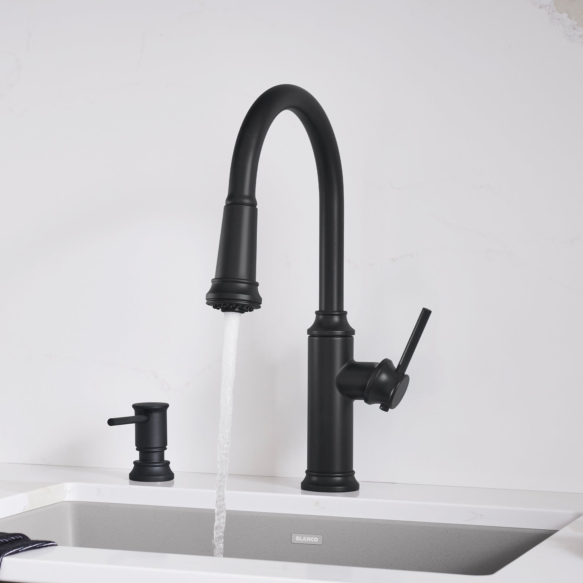 Matte black pull-down kitchen faucet with curved spout, single lever handle, and soap dispenser on white sink.