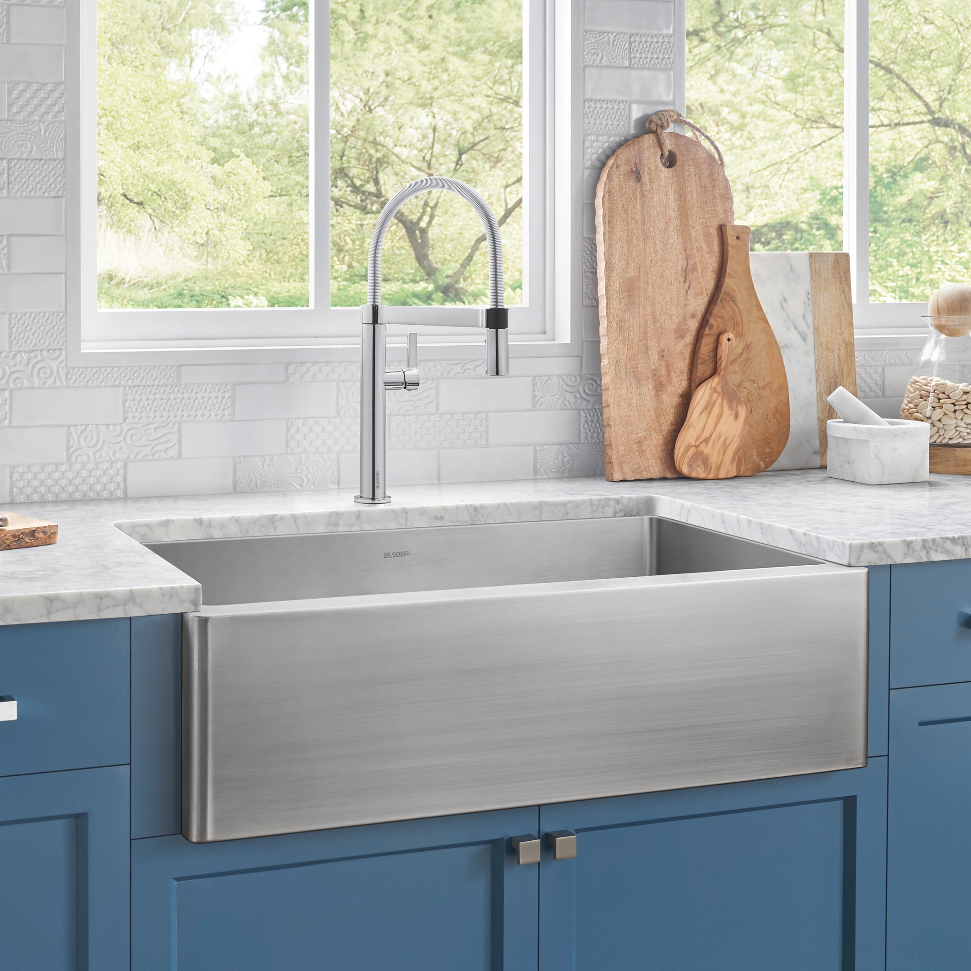 Stainless steel single apron-front sink with brushed finish mounted on blue cabinet base below marble countertop.