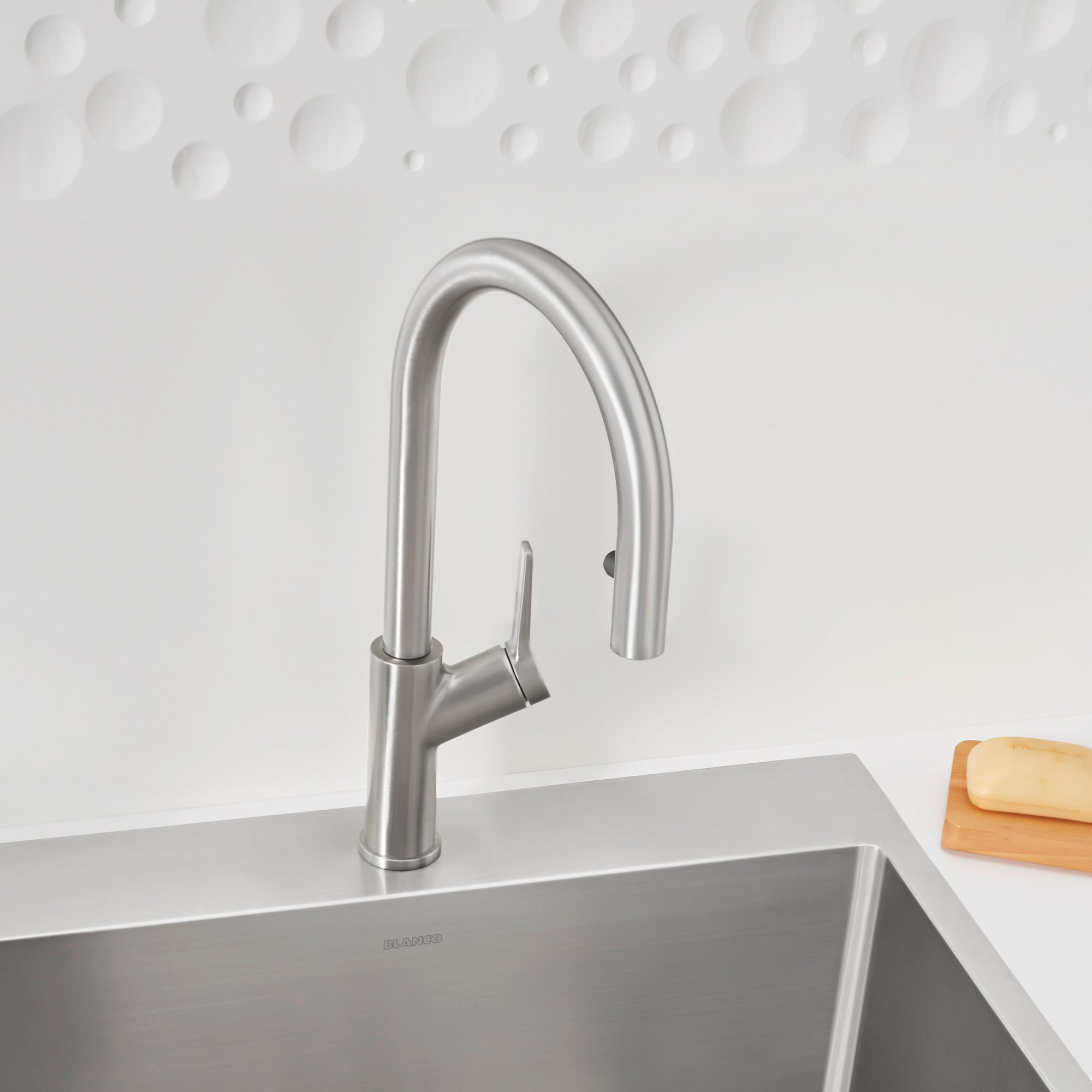 Stainless steel pull-down kitchen faucet with curved spout mounted on sink countertop.
