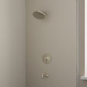 Brushed nickel shower set with round showerhead, circular valve trim, and tub spout mounted on tile wall.