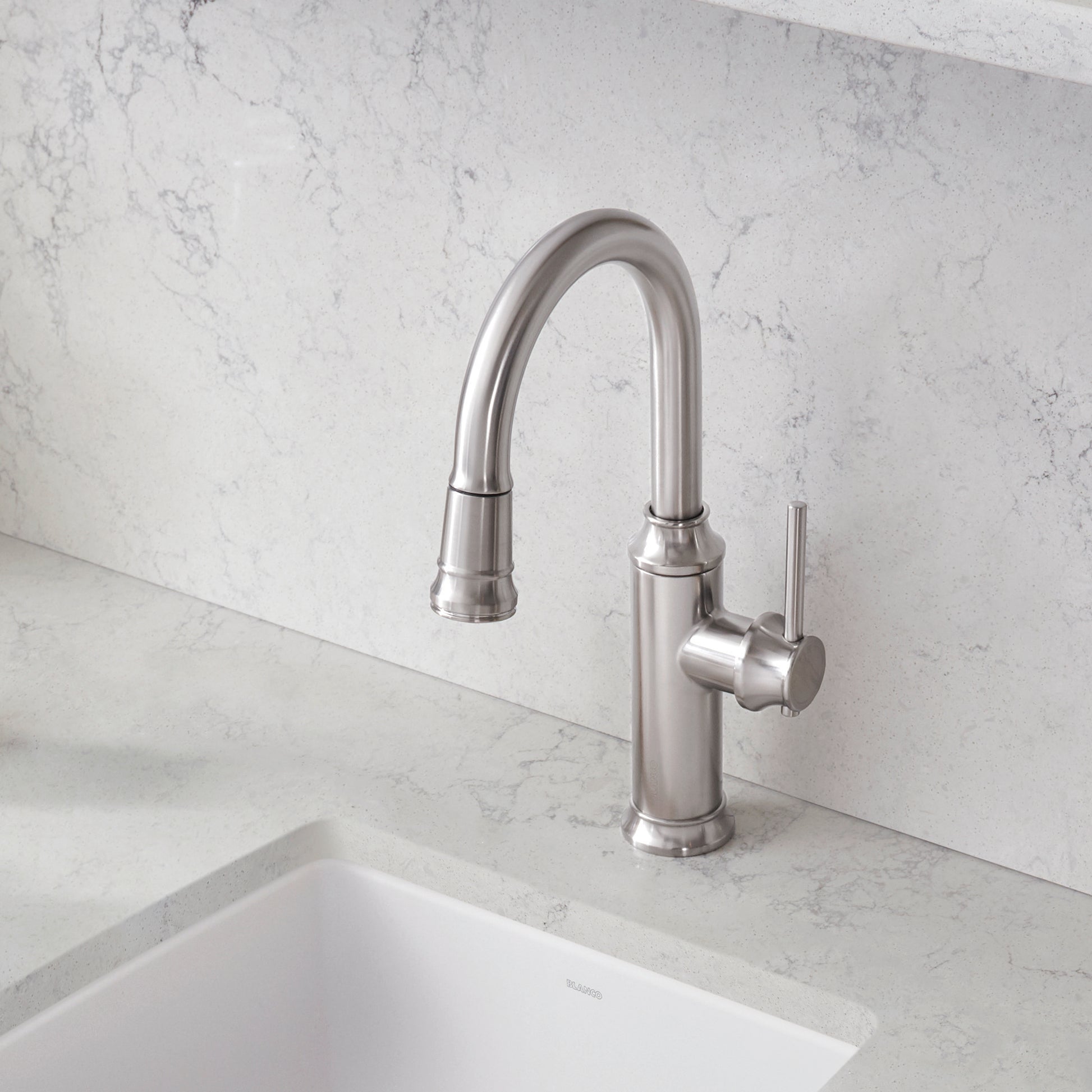 Stainless steel pull-down kitchen faucet with curved spout and single lever handle mounted on marble backsplash above white s
