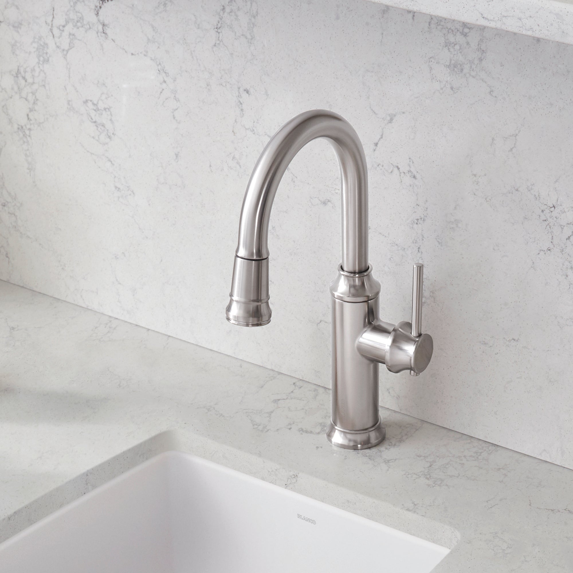 Stainless steel pull-down kitchen faucet with curved spout and single lever handle mounted on marble backsplash above white s