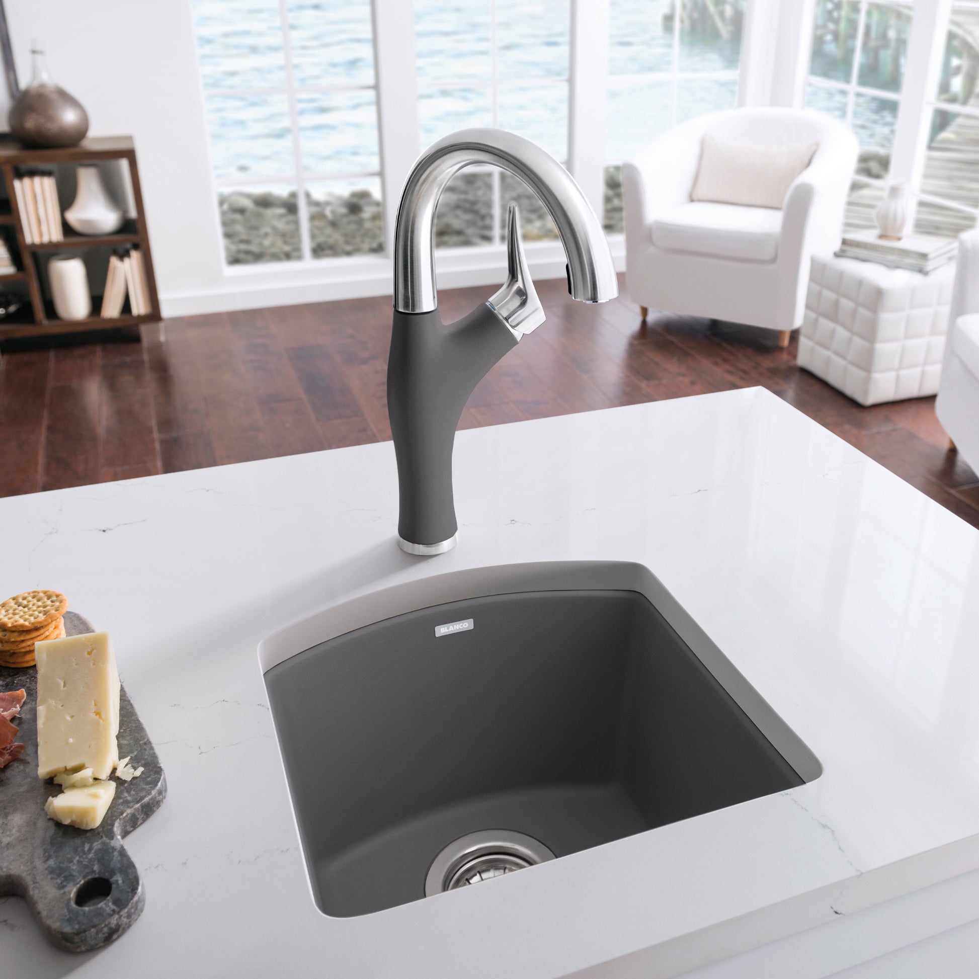 Dark gray composite bar sink with chrome pull-down faucet installed in white countertop.