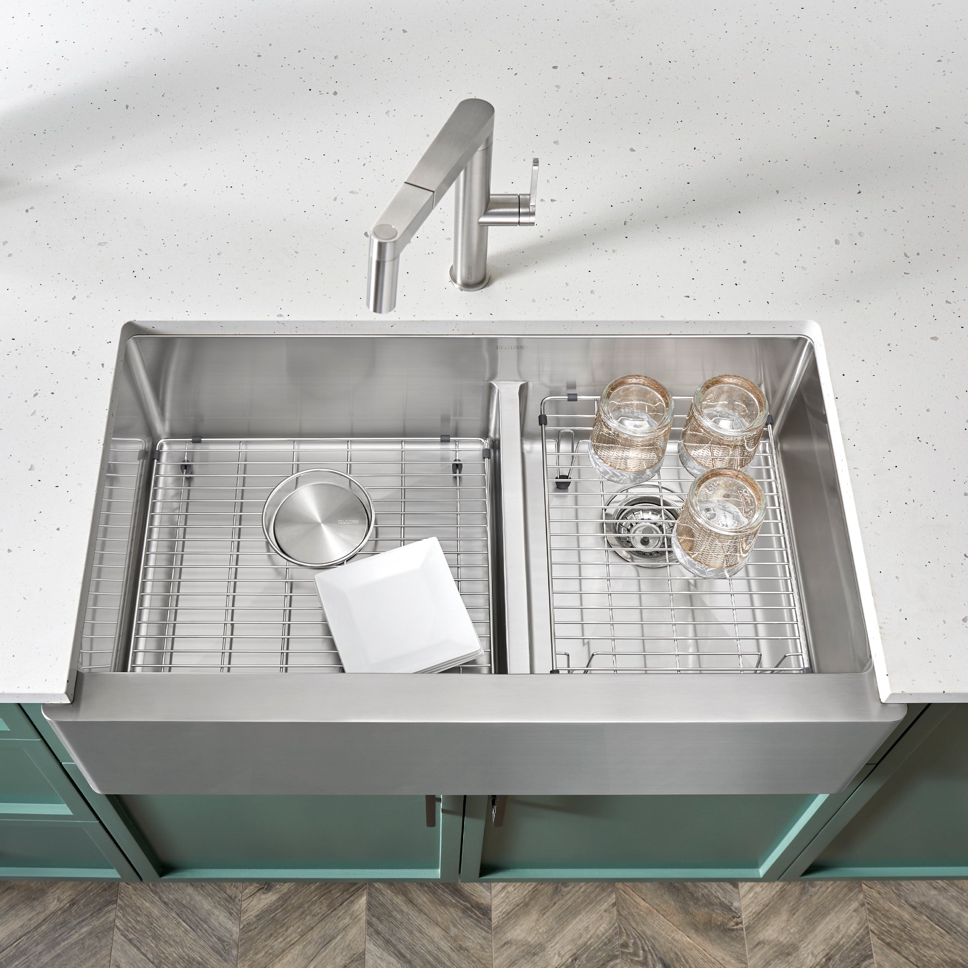 Stainless steel apron front sink with two compartments separated by low divider, including grids and faucet.