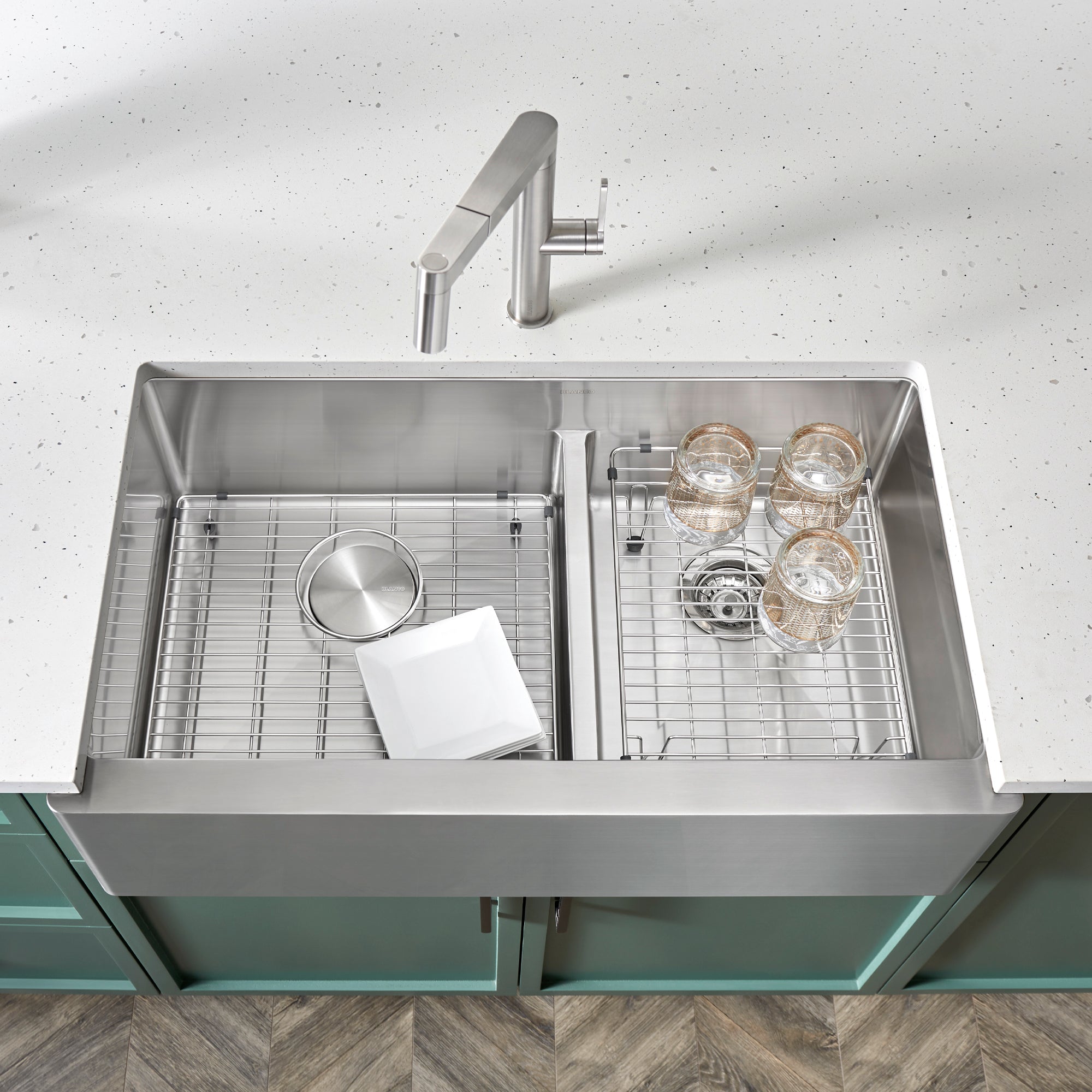 Stainless steel sink grid with parallel bars dividing double bowl farmhouse sink into sections, displayed with dishes and gla