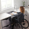 Woman in wheelchair at desk with single bowl stainless steel sink mounted at accessible height.