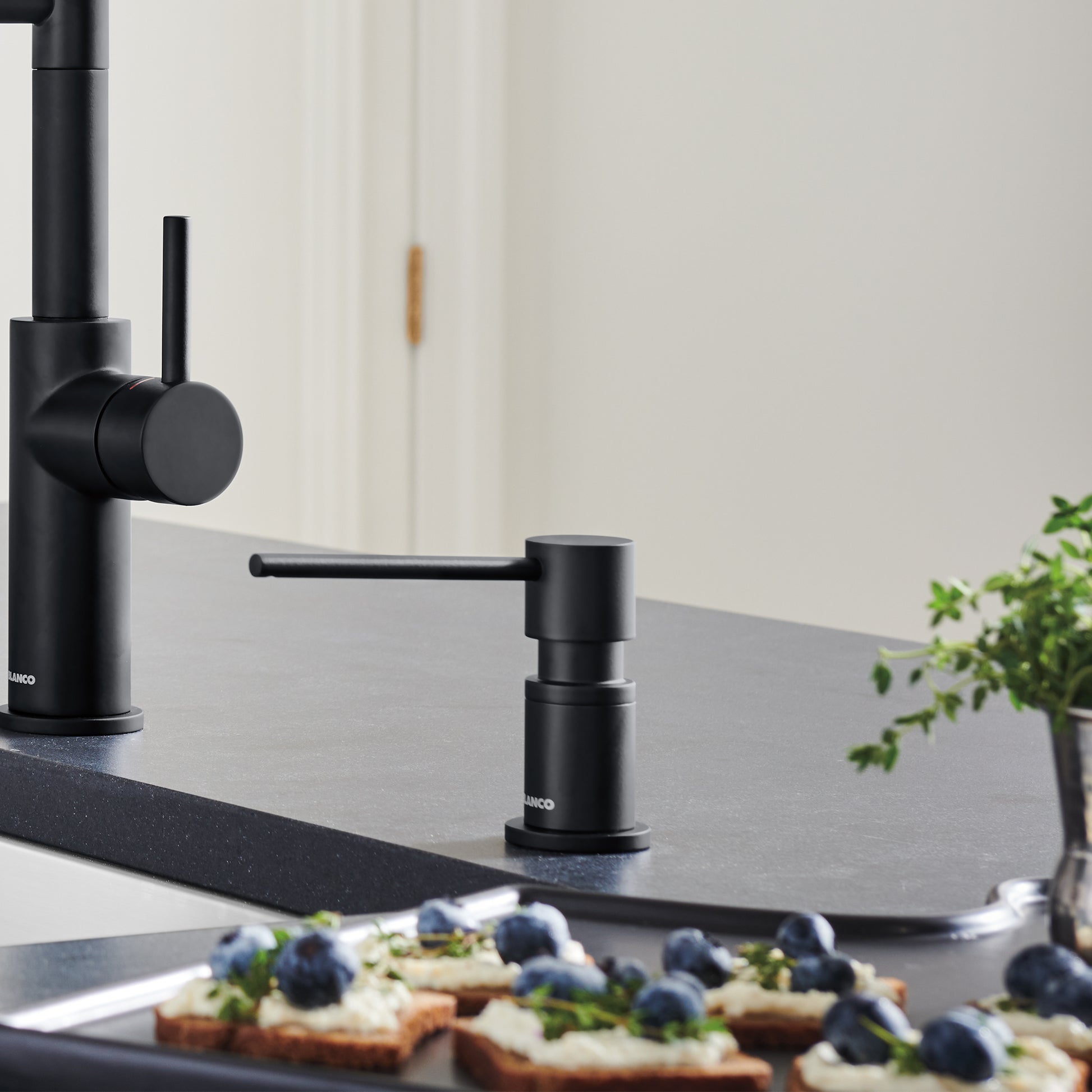 Matte black cylindrical soap dispenser with pump mechanism on kitchen countertop next to faucet.