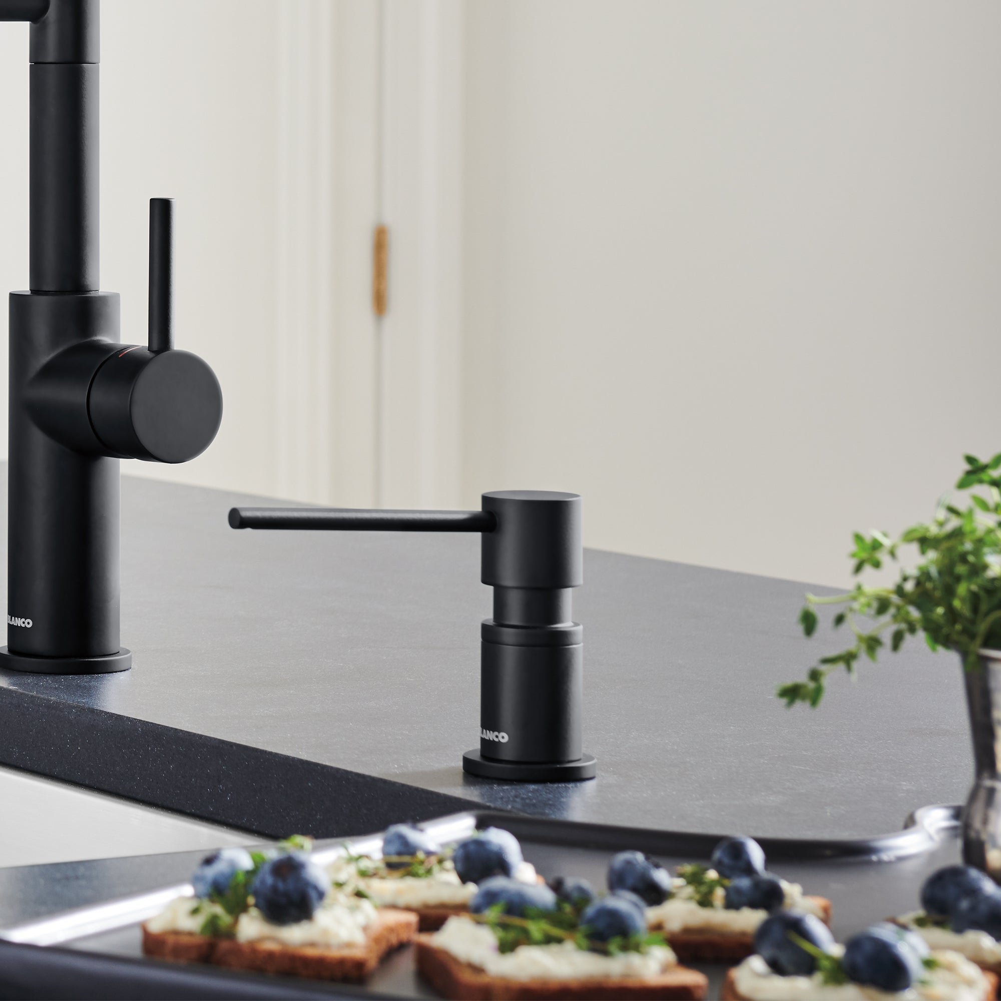 Matte black cylindrical soap dispenser with pump mechanism on kitchen countertop next to faucet.