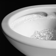 Bone-colored elongated toilet bowl with water flowing during flush cycle.