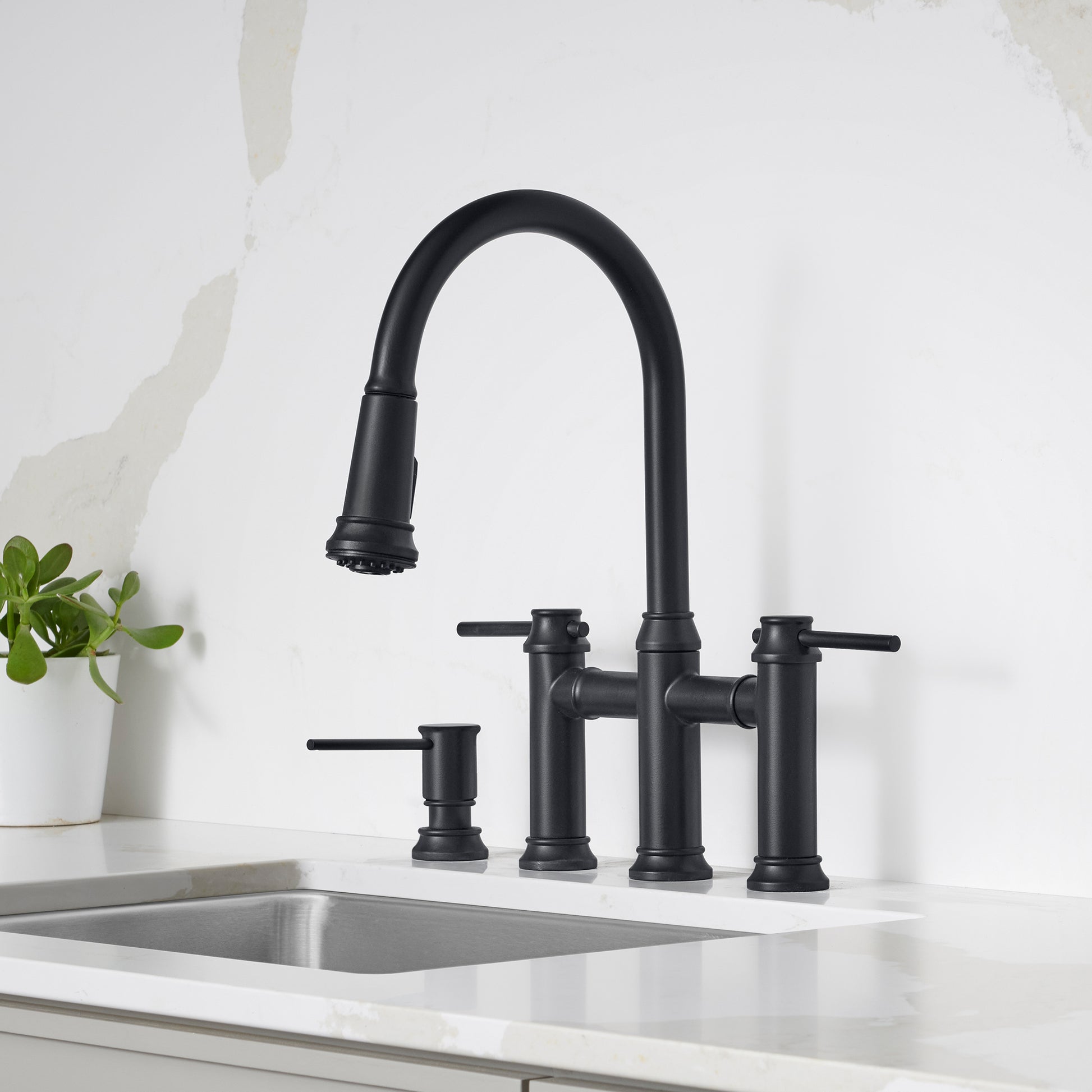 Matte black bridge faucet with pull-down sprayer, two lever handles, and soap dispenser on white countertop.